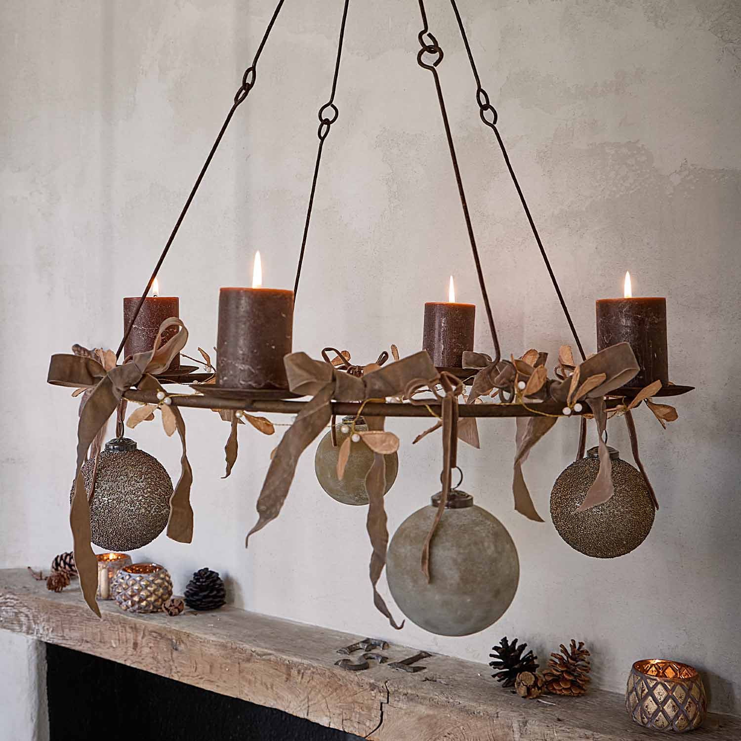 Chandelier suspendu en métal avec quatre bougies brunes et boules décoratives sur fond mural