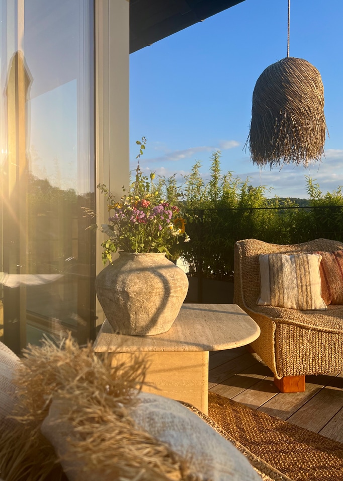 Balcon chaleureux avec fauteuil en osier, table en pierre et vase de fleurs sous une lumière naturelle