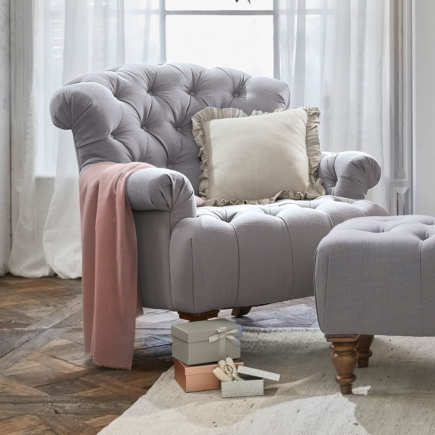 Fauteuil Springfield Fauteuil gris en tissu avec repose-pieds assorti, coussin crème et plaid rose dans un salon lumineux