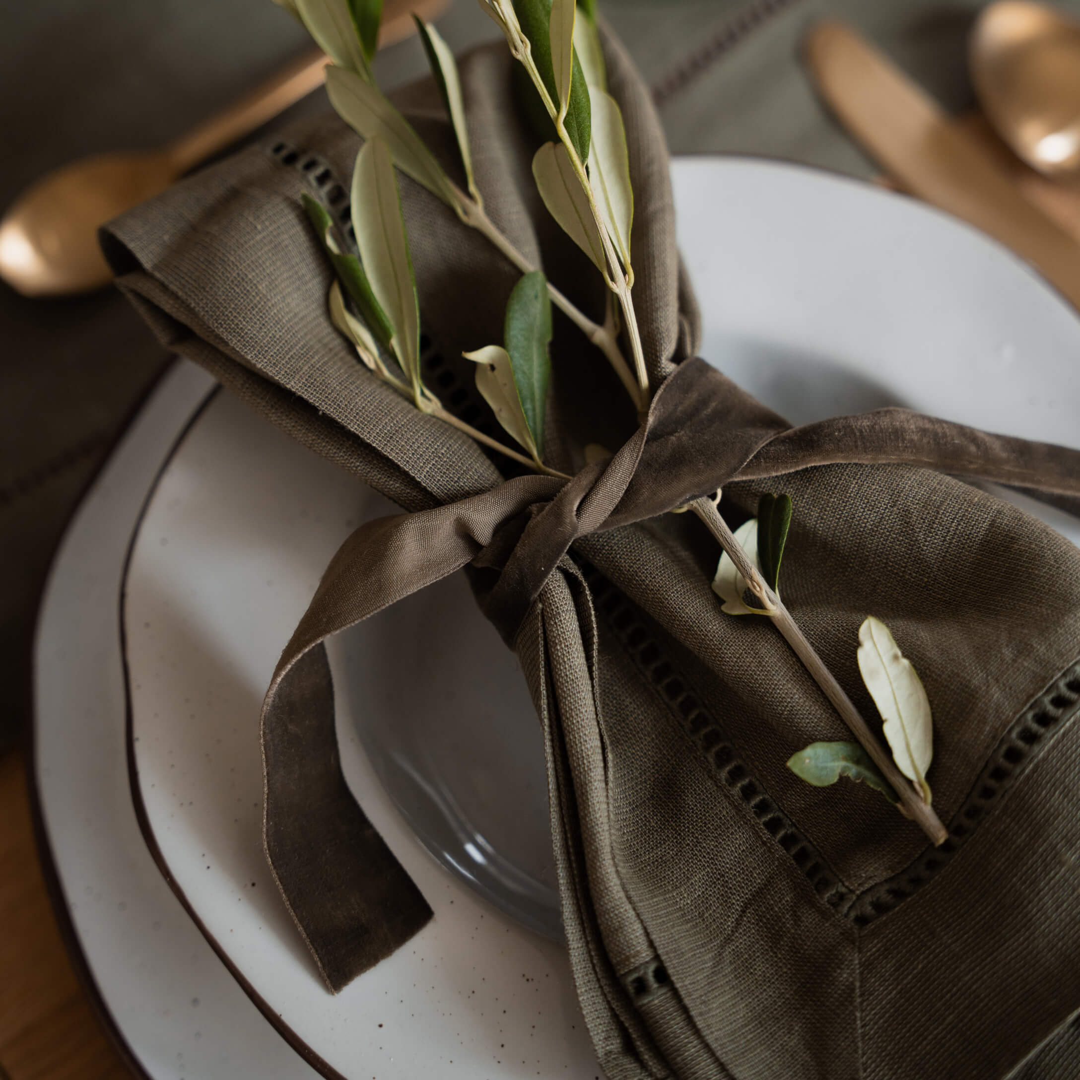 Serviette en lin marron avec branches vertes sur assiette blanche pour décoration de table
