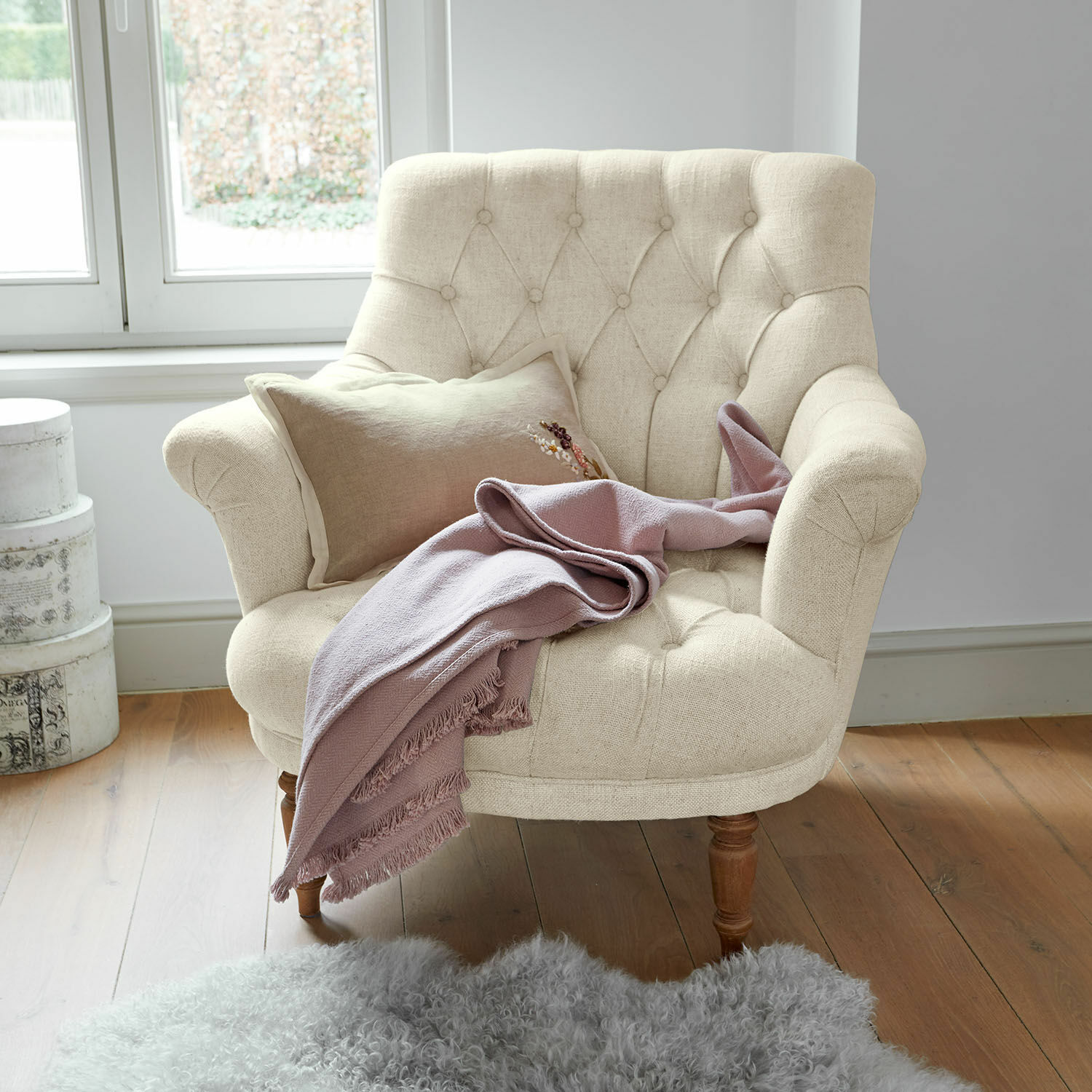 Fauteuil Rive Dorée Fauteuil beige en tissu avec pieds en bois, couverture rose et tapis en peau d'agneau sur parquet