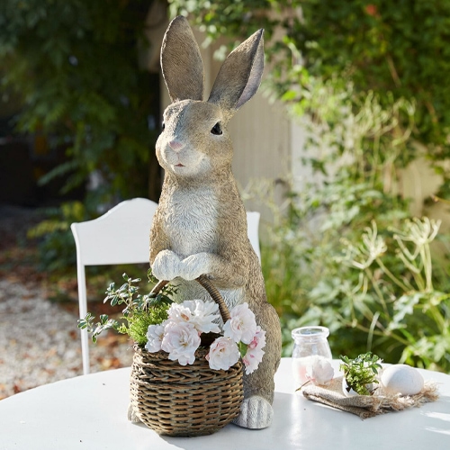 Lapin décoratif en matière synthétique couleur naturelle avec panier en osier et fleurs sur table de jardin