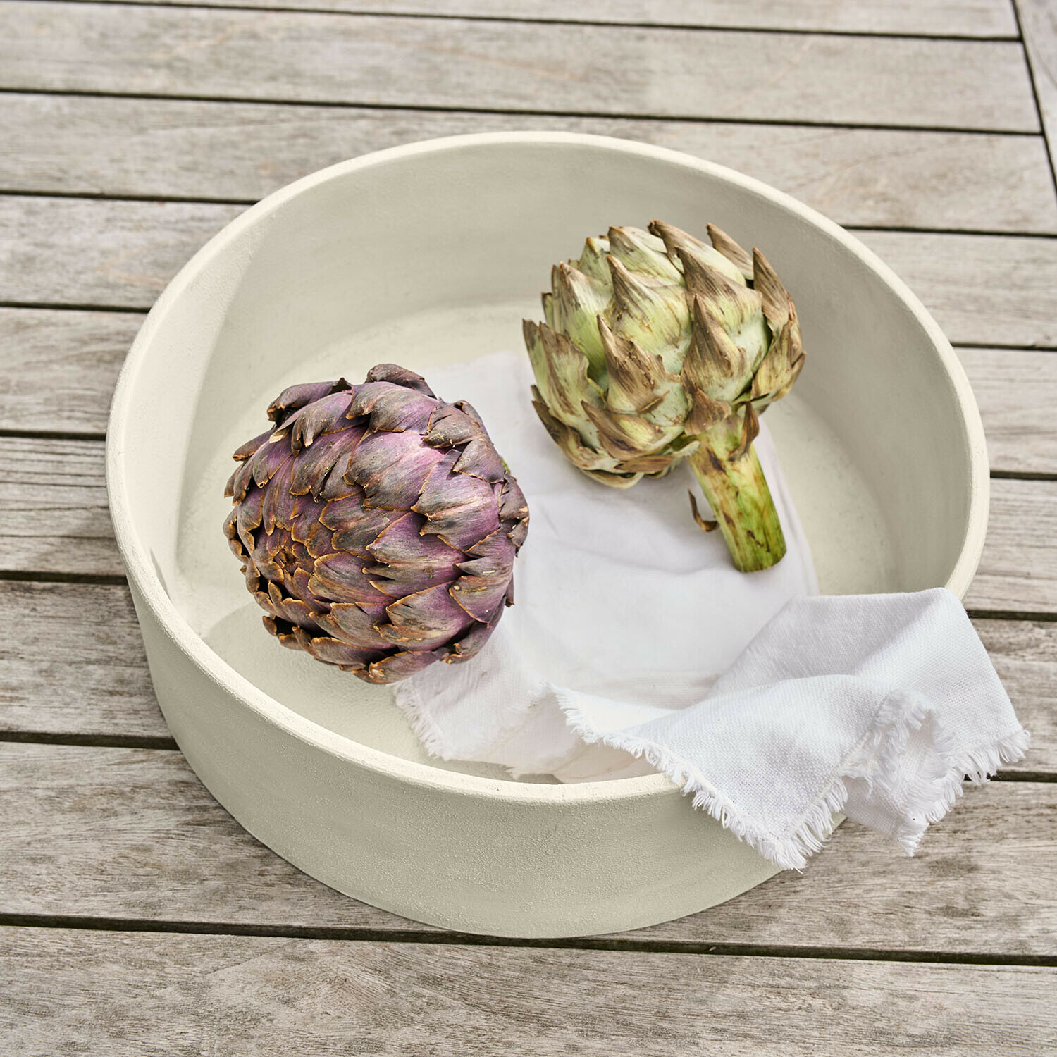 Coupe Islene Bol en céramique crème avec deux artichauts et un linge blanc sur une table en bois