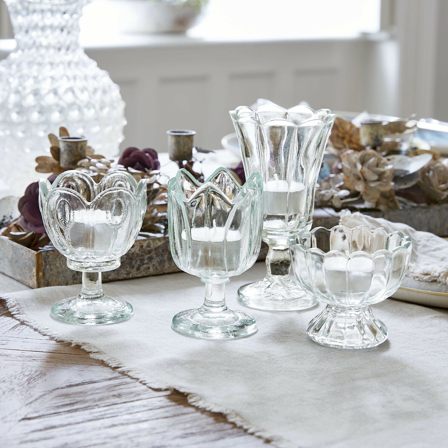 Lot de 4 photophores Amisette Ensemble de quatre bougeoirs en verre transparent de formes variées sur une nappe claire