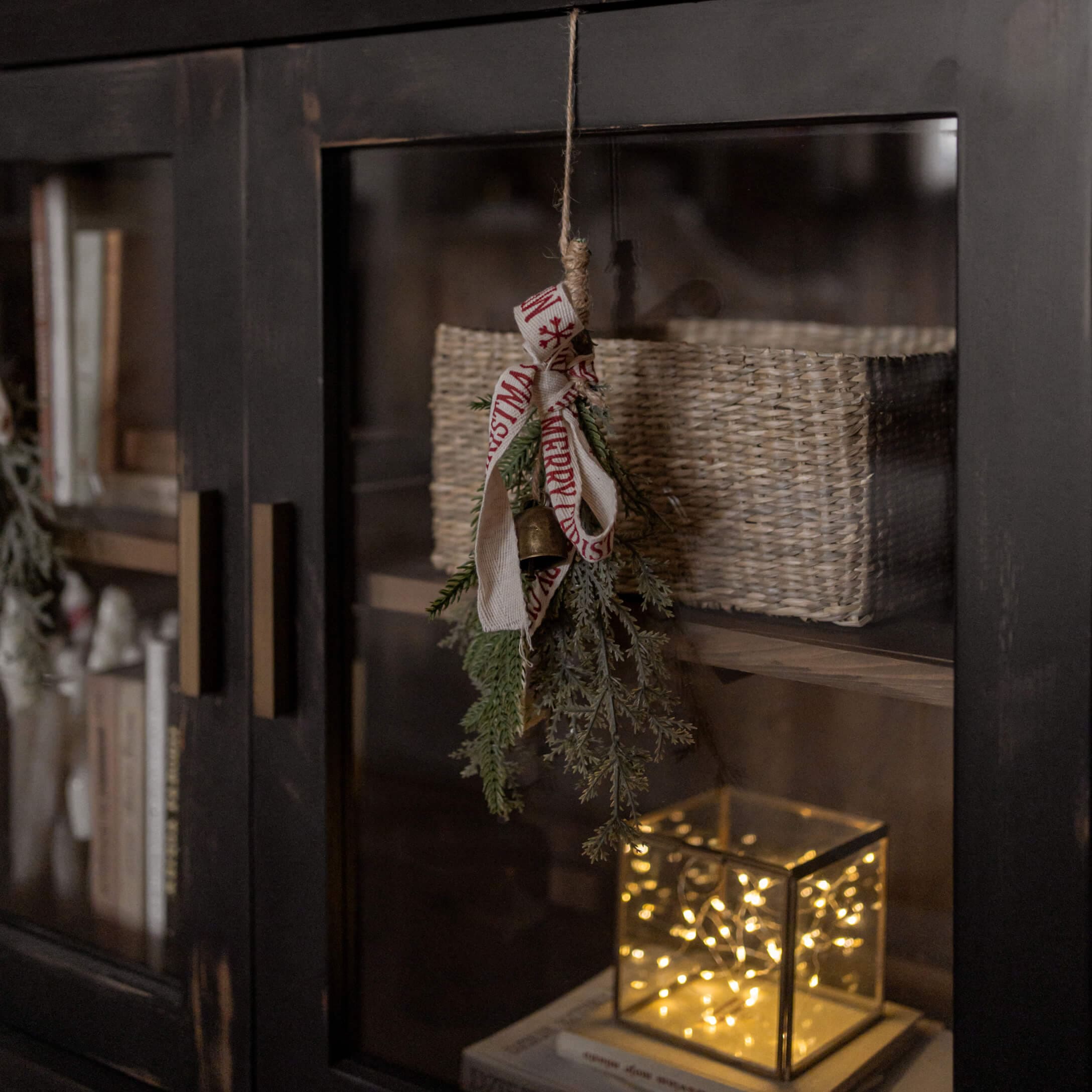 Décoration de Noël avec branches vertes, clochette et ruban sur meuble noir avec panier et lampe LED