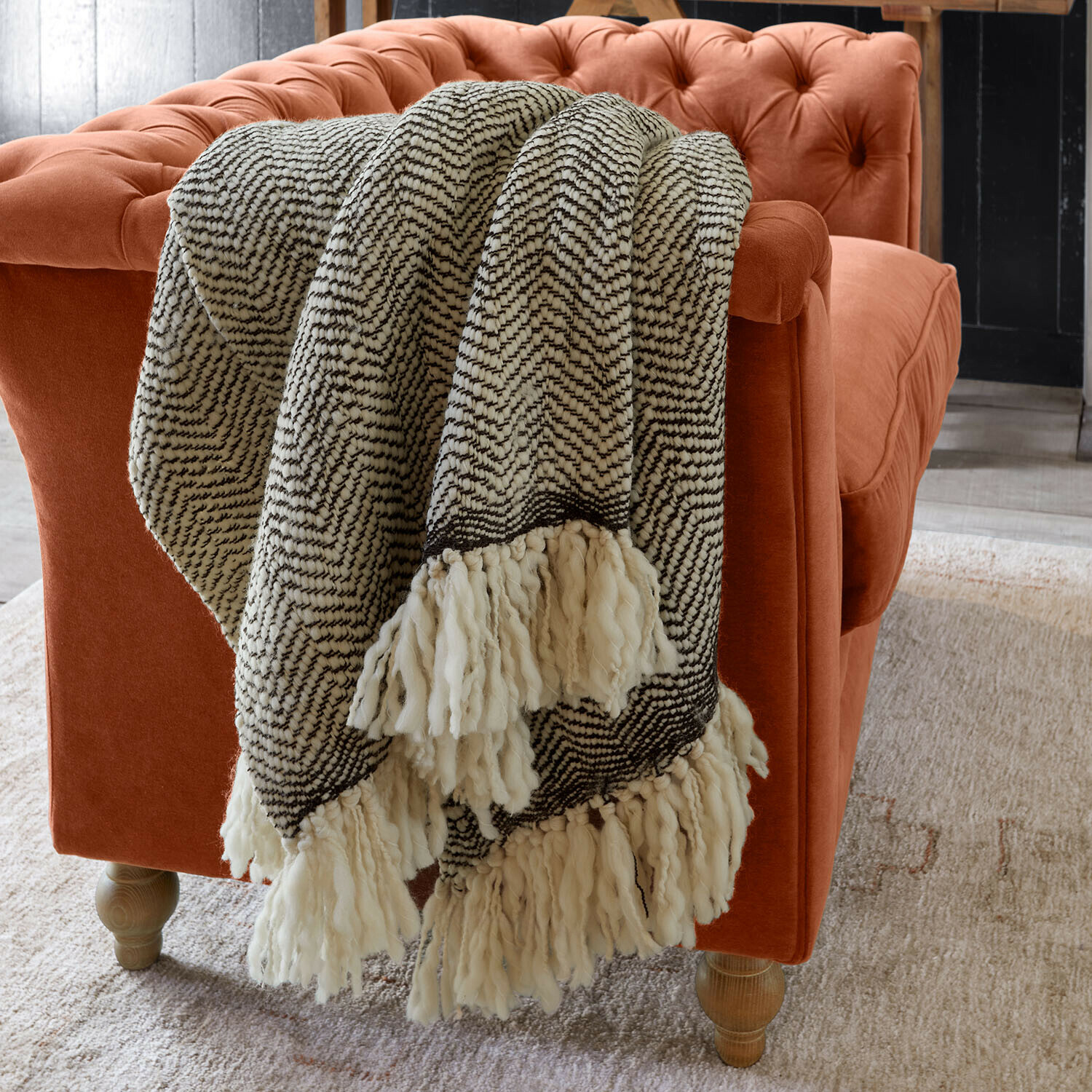 Plaid Kerenza Plaid doux à franges noir et blanc posé sur un canapé en velours orange dans un salon moderne