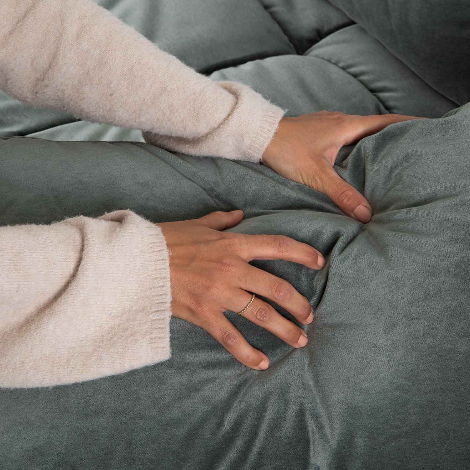 Mains touchant un tissu d'ameublement en velours vert doux avec capitonnage, textile confortable