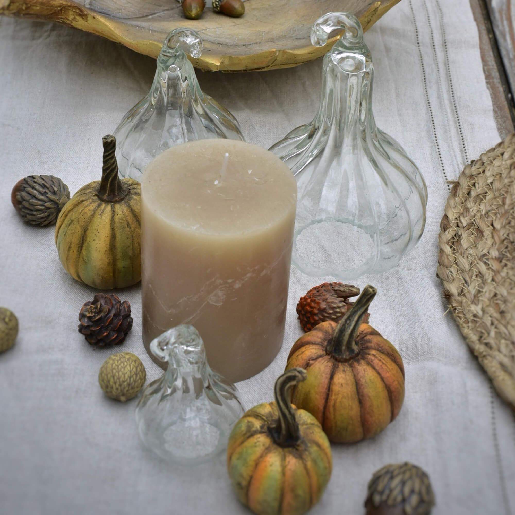 Bougie beige entourée de citrouilles en verre transparent et petites décorations sur tissu lin