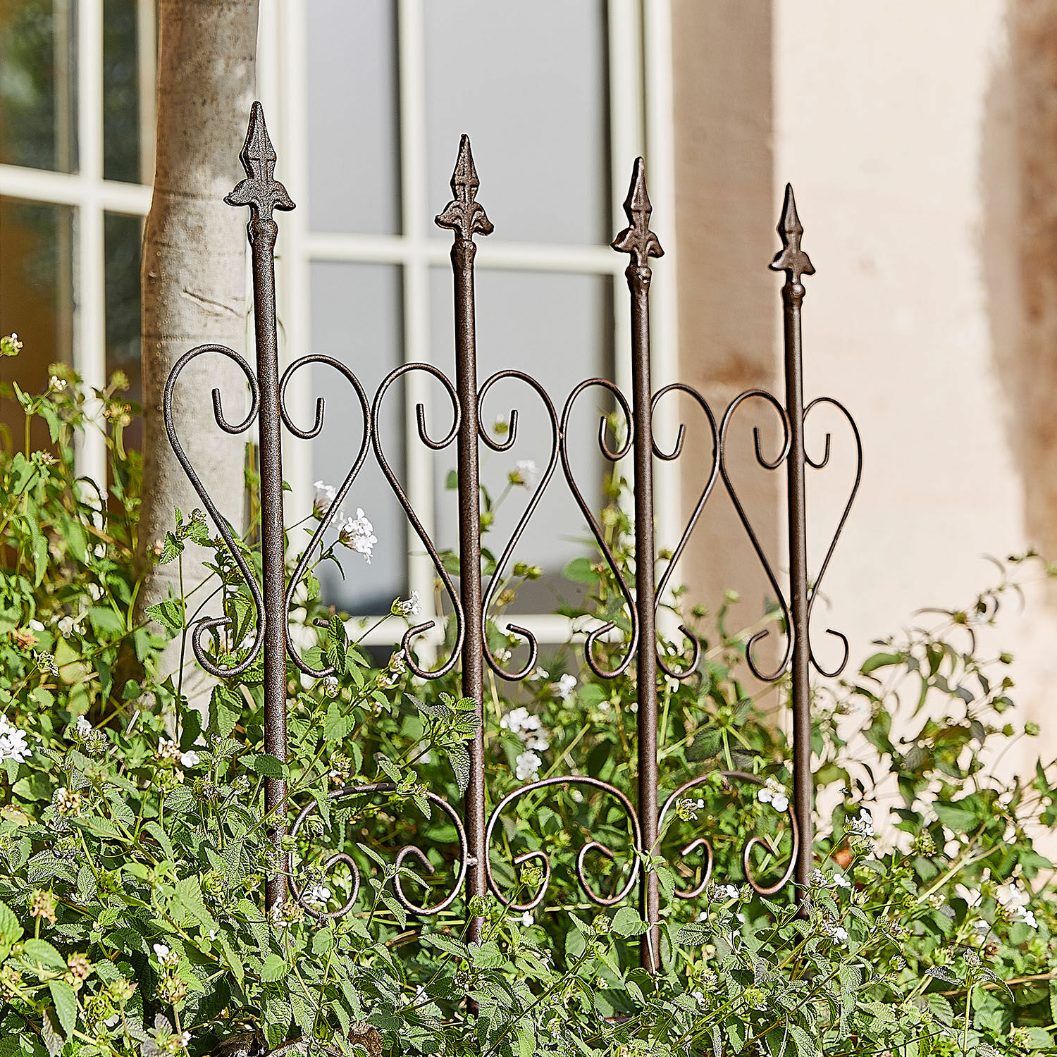 Treillage Nectarise Clôture de jardin en métal brun rouille avec motif cœur, entourée de plantes vertes et fleurs blanches