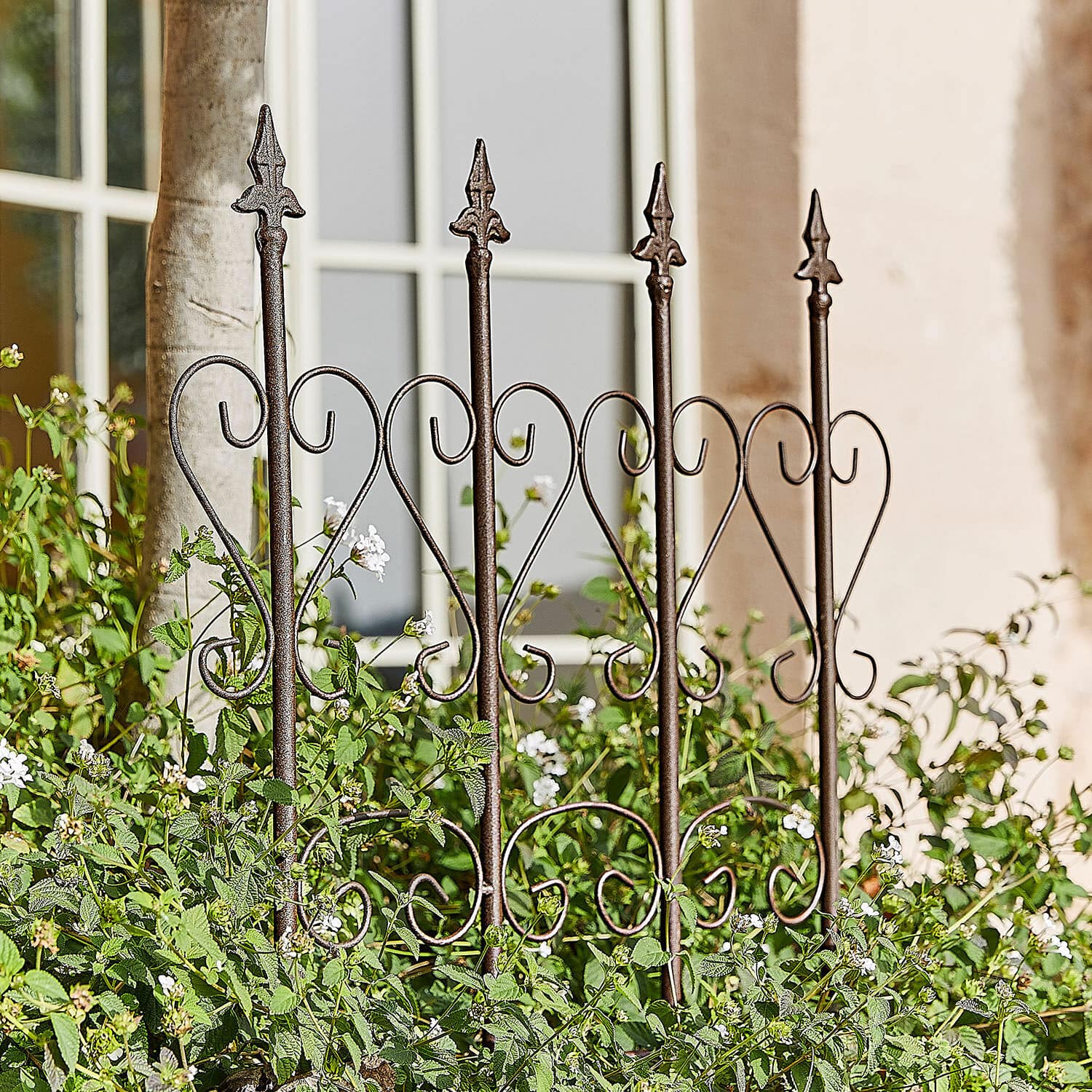 Treillage Nectarise Clôture de jardin en métal brun rouille avec motif cœur, entourée de plantes vertes et fleurs blanches