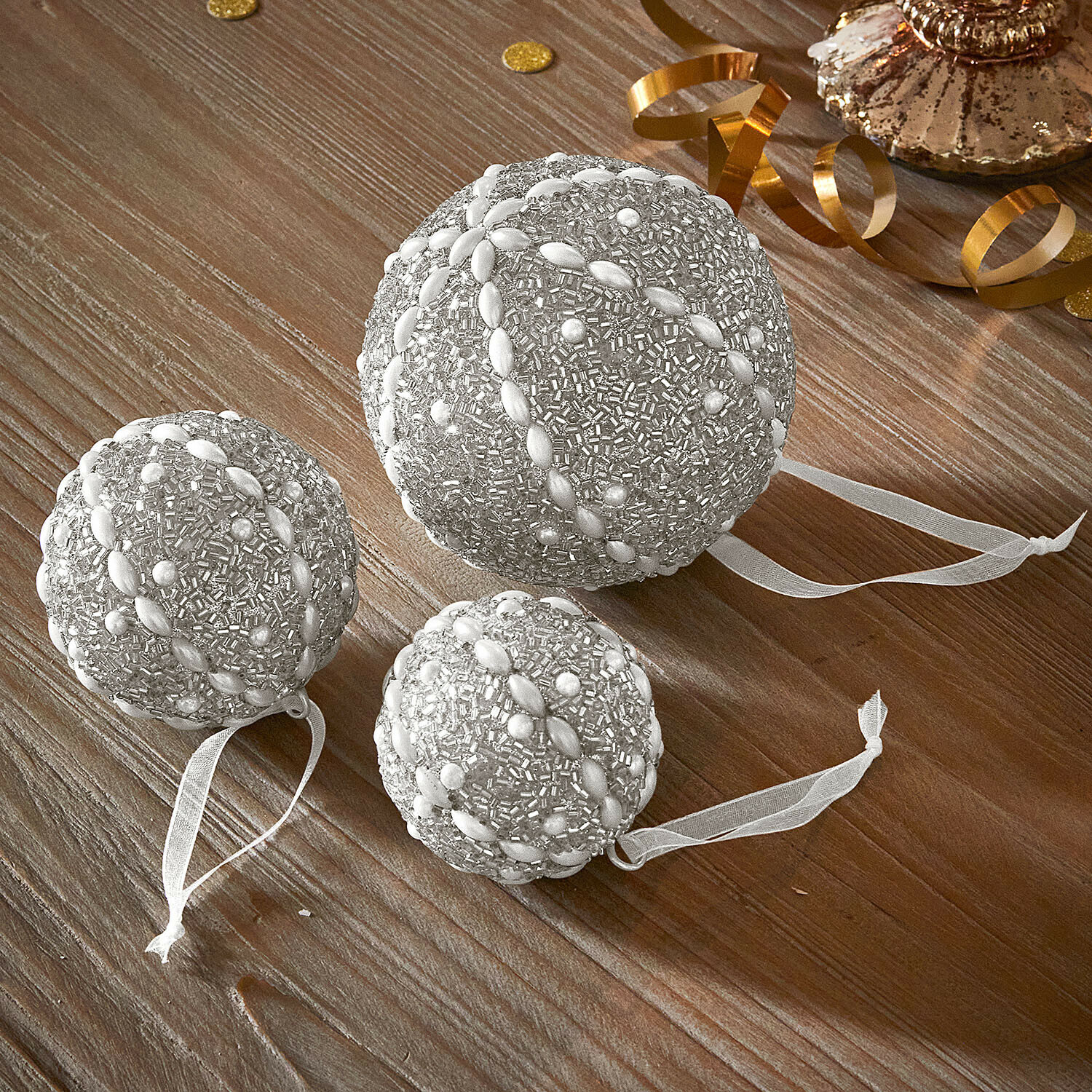 Lot de 3 boules de Noël Maelvik Ensemble de trois boules de Noël argentées ornées de perles avec rubans sur table en bois