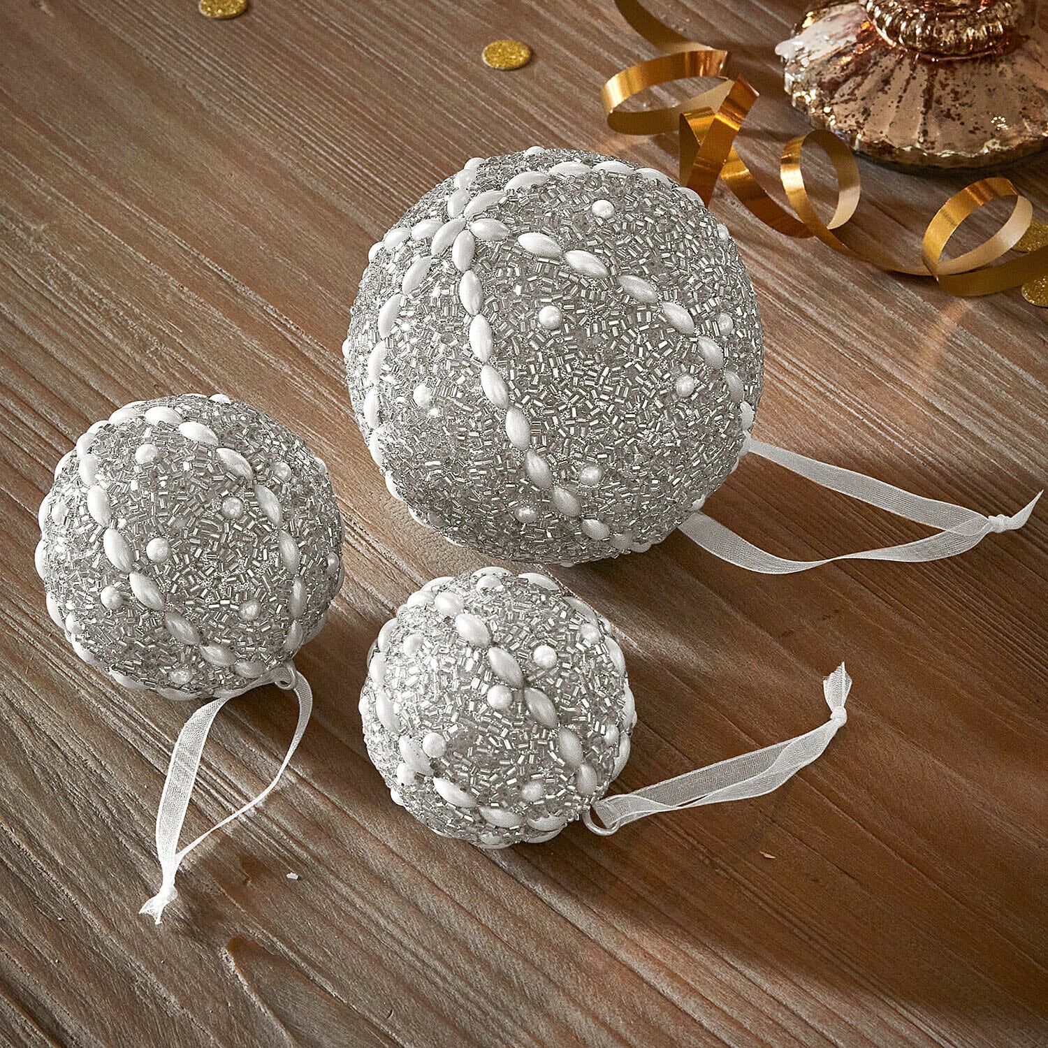 Lot de 3 boules de Noël Maelvik Ensemble de trois boules de Noël argentées ornées de perles avec rubans sur table en bois