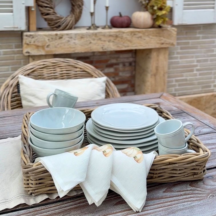 Service de vaisselle en céramique gris clair avec assiettes, bols et tasses dans un panier en osier sur une table en bois