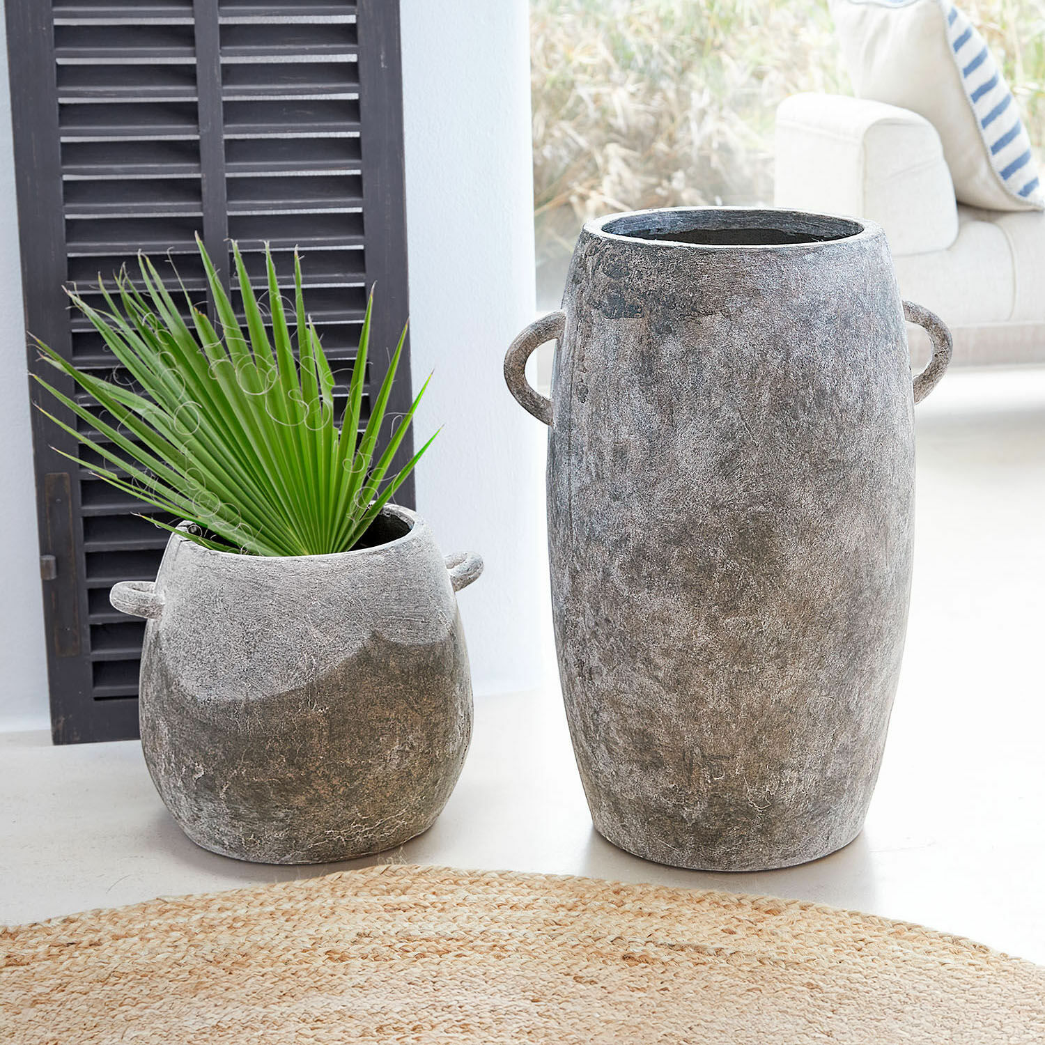 Lot de 2 cache-pots Cœuron Deux pots en béton gris de tailles différentes avec poignées, l'un avec une feuille verte, décoration intérieure