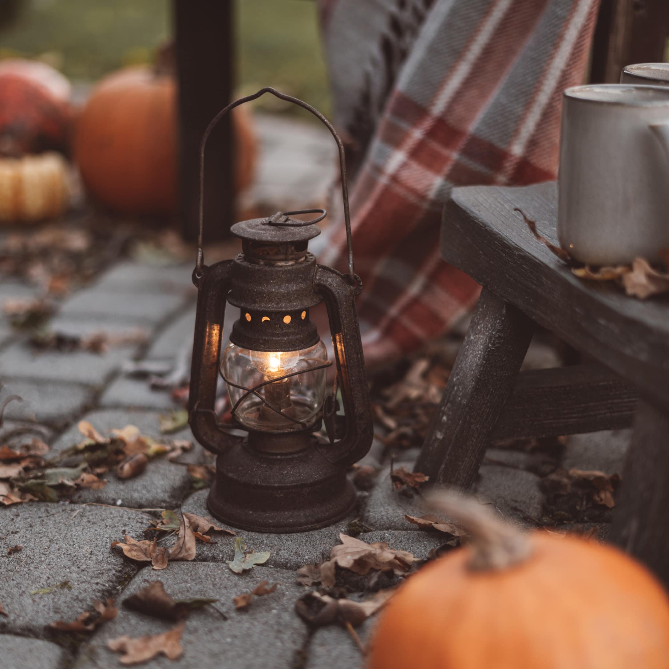 Lanterne en métal rustique avec lumière chaude sur patio pavé avec citrouilles et plaid