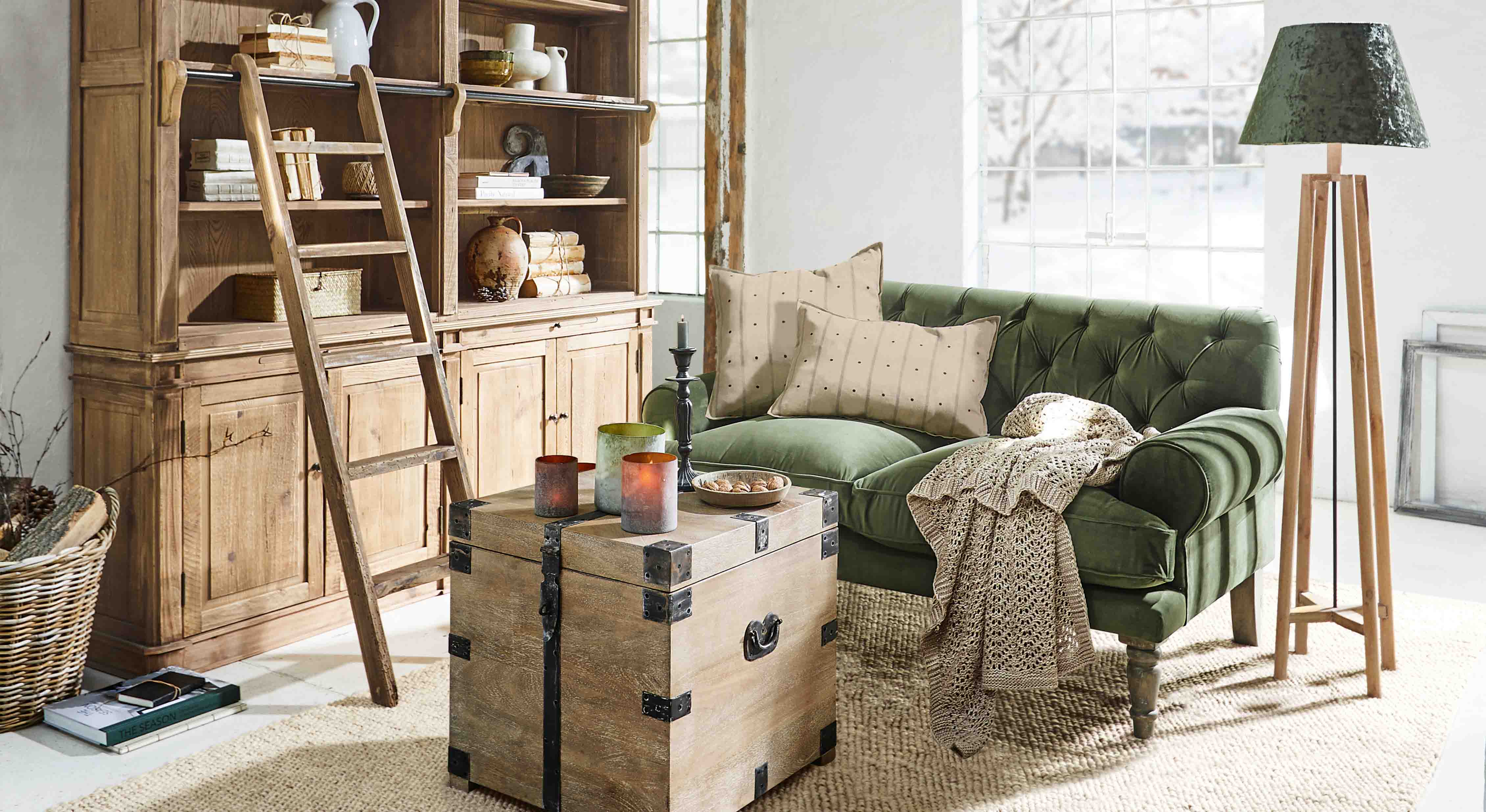 Salon chaleureux avec canapé vert en velours, bibliothèque en bois et lampe sur pied en bois naturel
