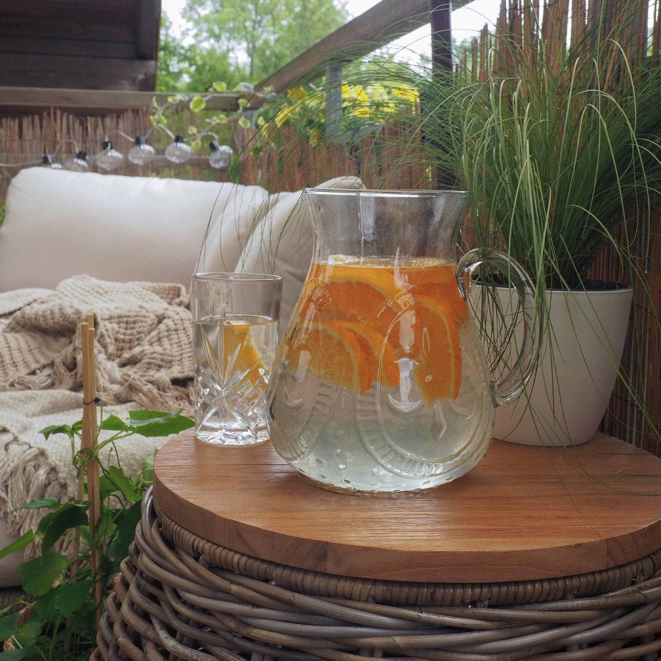 Carafe en verre avec eau et tranches d'orange sur table en bois sur terrasse avec plantes