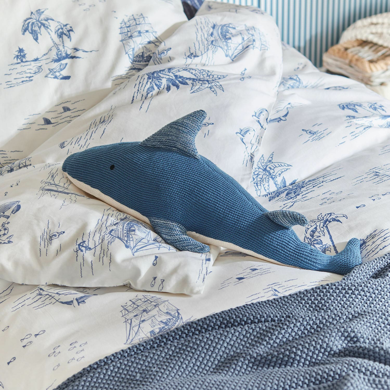 Peluche Cheruboo Coussin tricoté bleu en forme de requin sur une literie blanche à motifs marins bleus