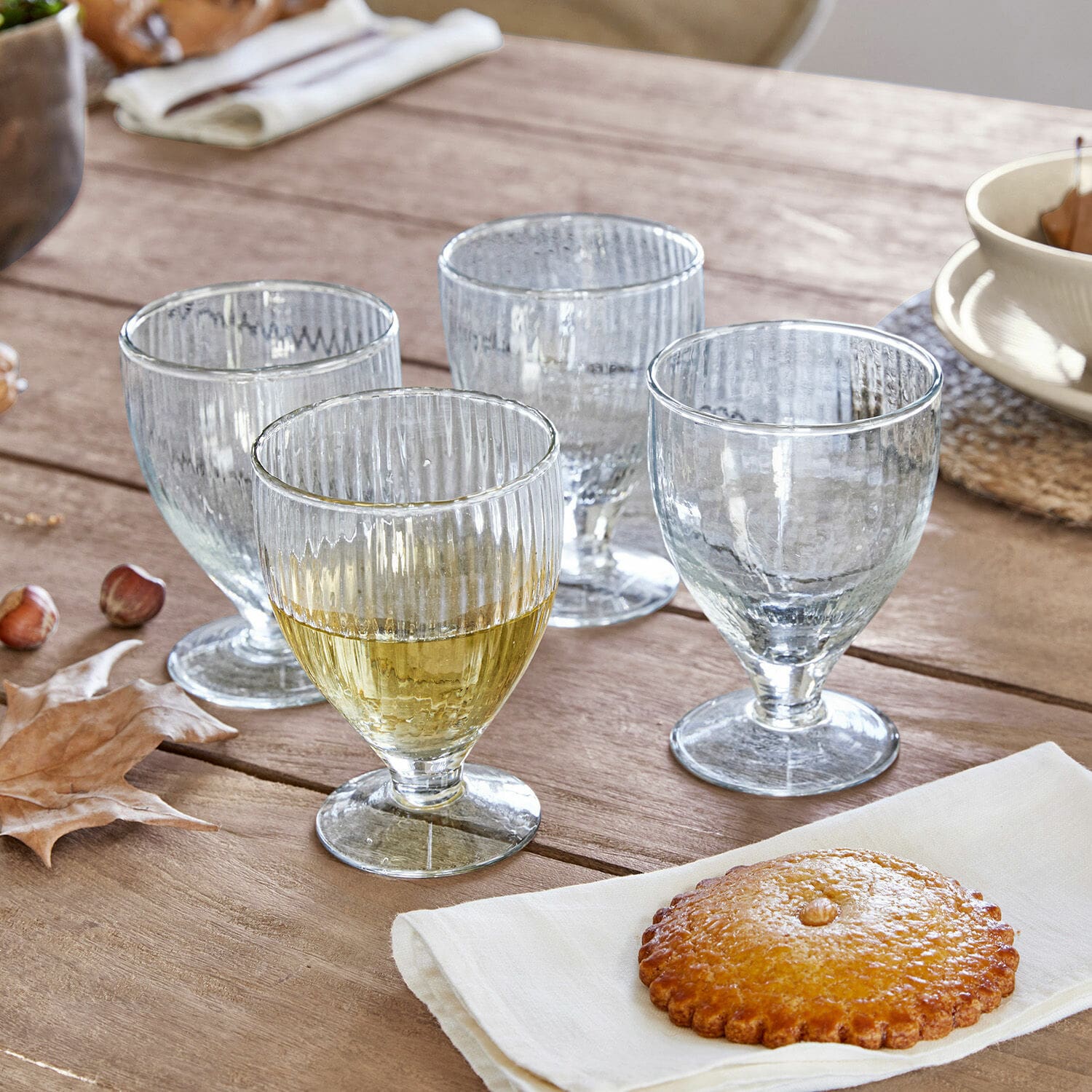 Lot de 4 verres Laredo Ensemble de quatre verres transparents en verre strié sur pied sur une table en bois avec un biscuit