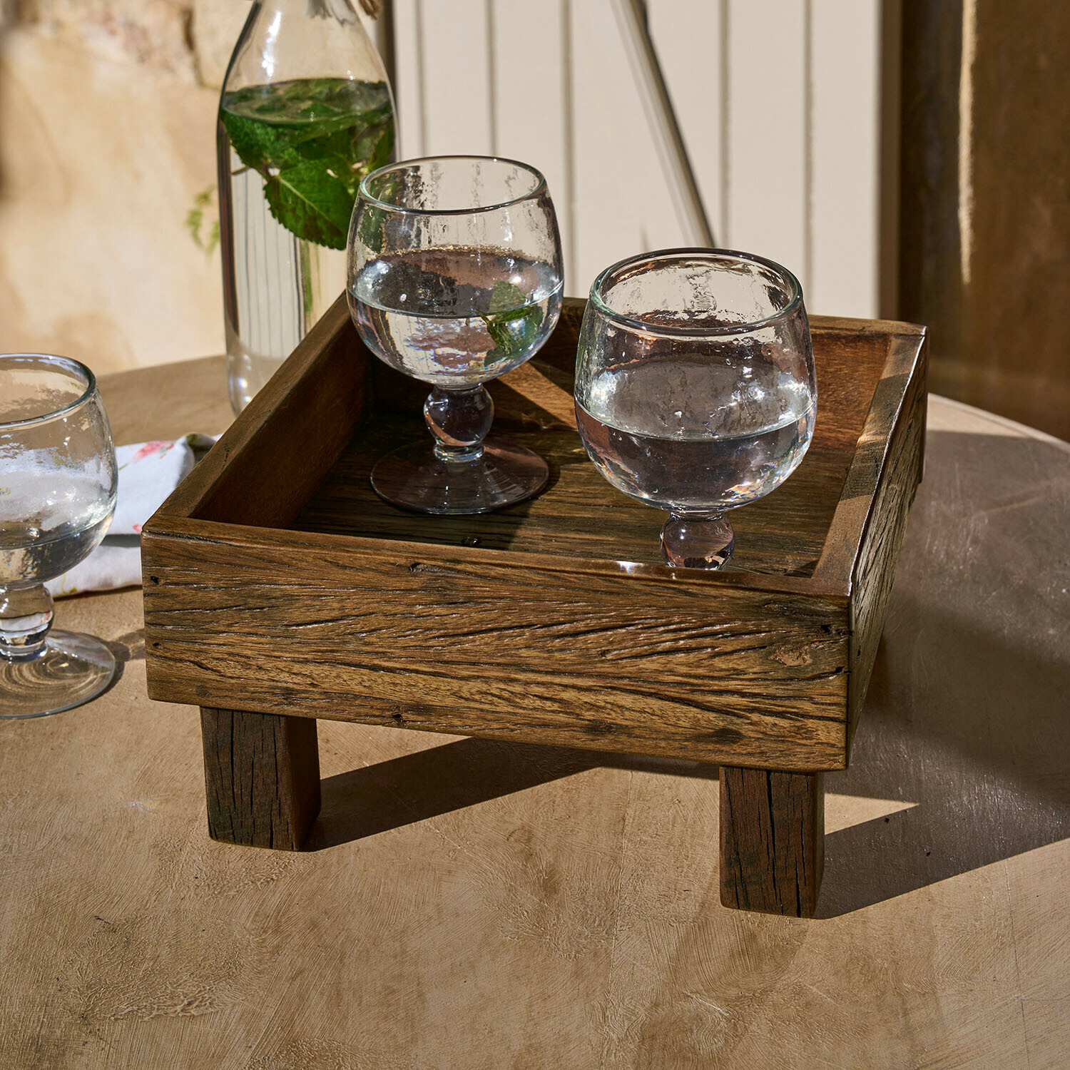 Plateau en bois foncé sur pieds avec deux verres d'eau et feuilles de menthe sur une table