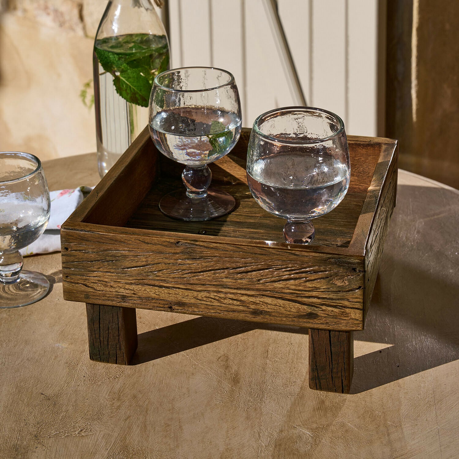 Plateau Oldmere Plateau en bois foncé sur pieds avec deux verres d'eau et feuilles de menthe sur une table