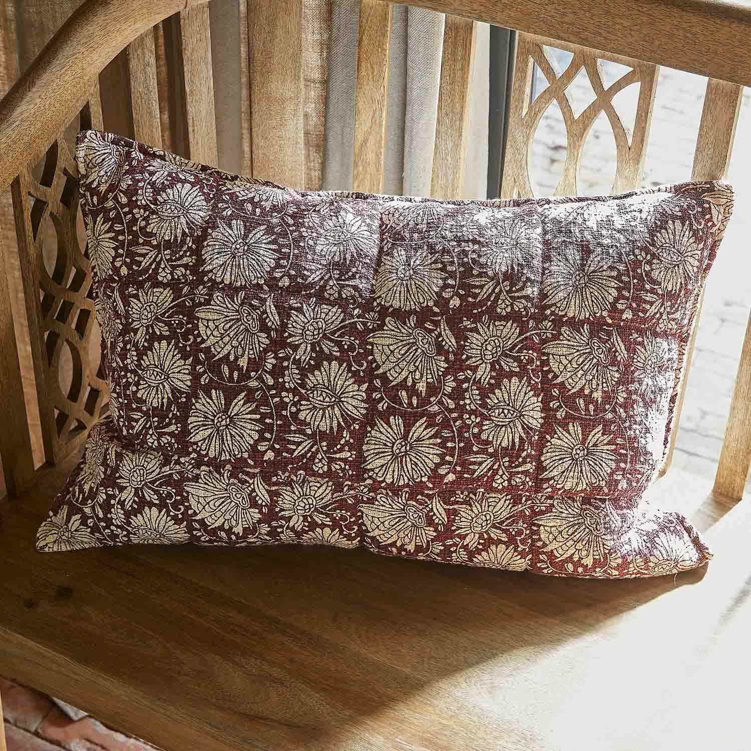 Coussin décoratif en coton bordeaux avec motif floral crème posé sur un banc en bois