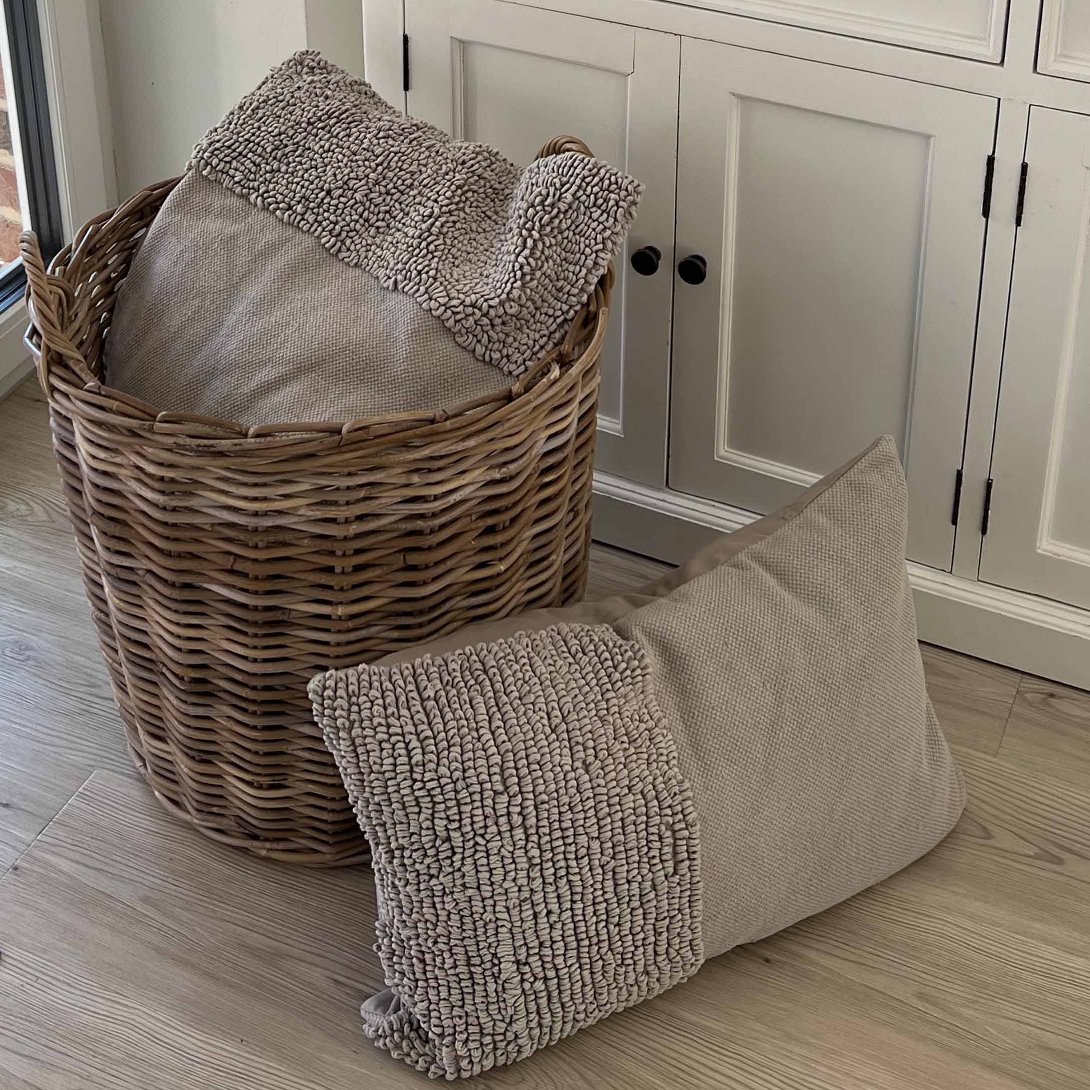 Coussin beige en tissu doux avec texture posé près d'un panier en osier sur un sol en bois