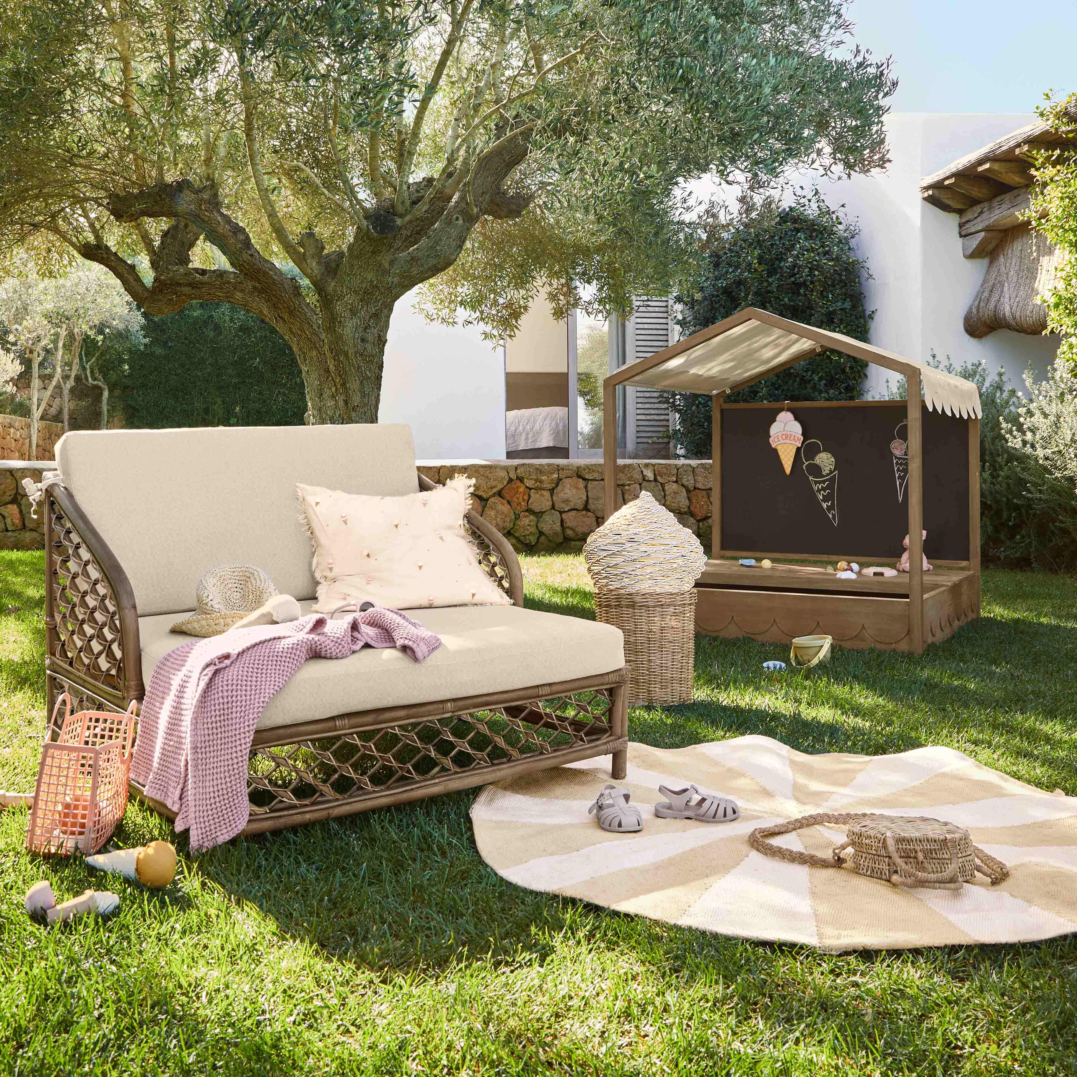 Mobilier de jardin en rotin avec coussins beige et maison de jeu pour enfants sur pelouse dans un jardin ensoleillé