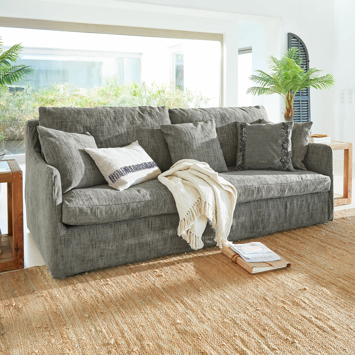 Canapé Shadowfield Canapé gris en tissu avec coussins et plaid crème sur tapis naturel dans un salon lumineux