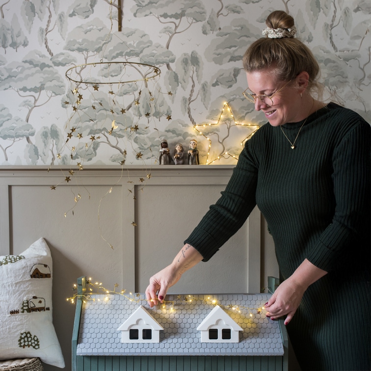 Femme décorant un coffre en bois gris avec des guirlandes lumineuses étoiles dans un intérieur chaleureux