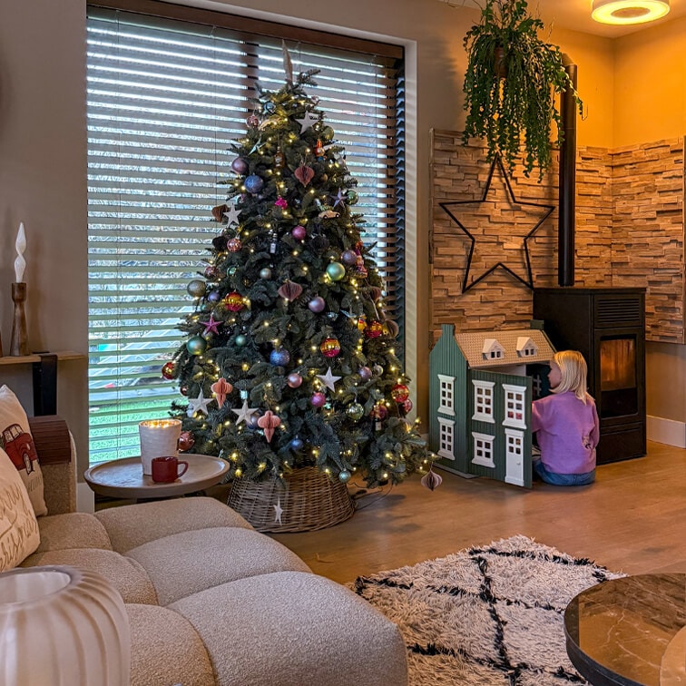 Salon chaleureux avec sapin de Noël décoré, canapé moelleux et enfant jouant avec une maison de poupée