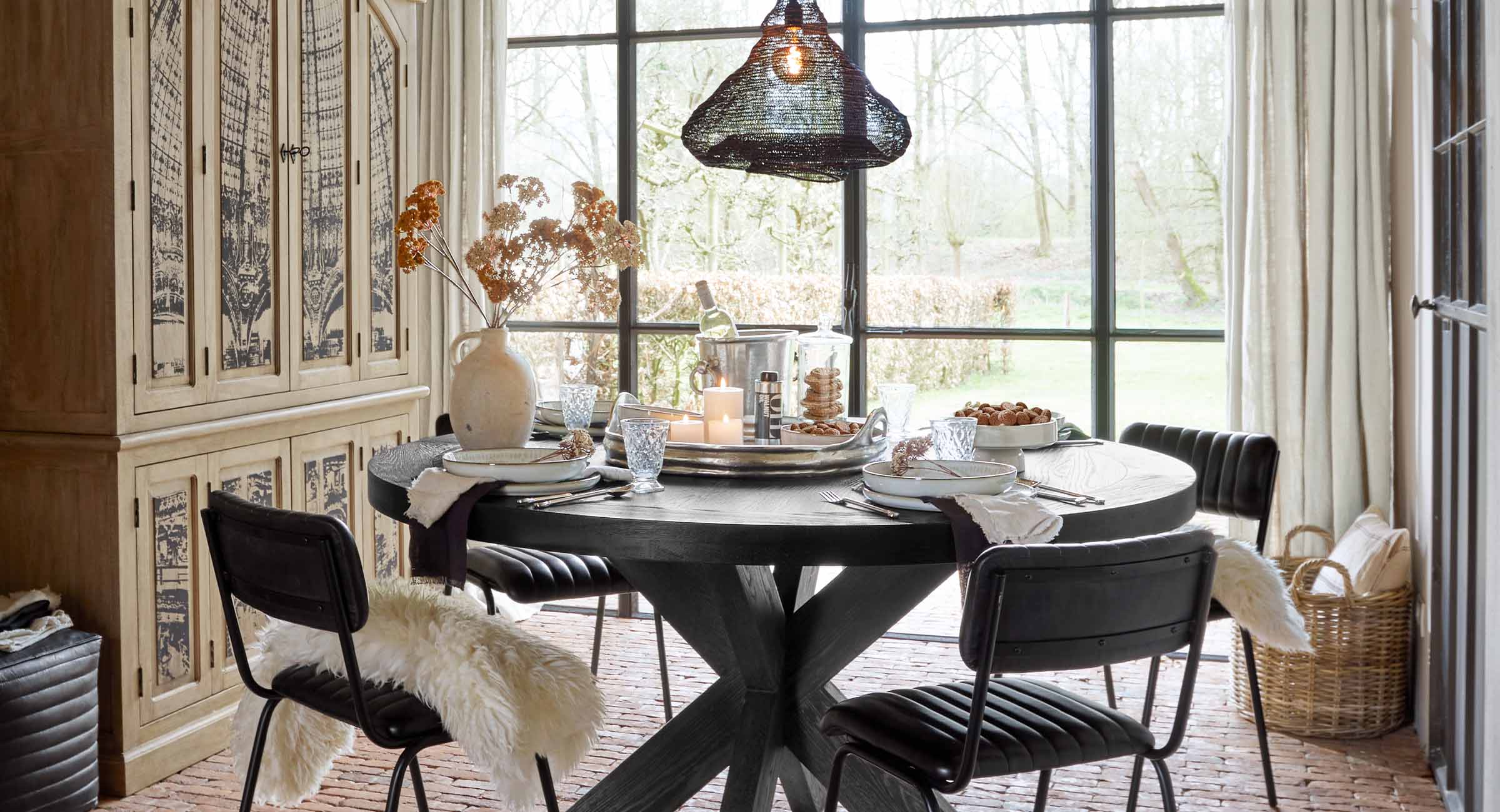 Salle à manger avec table ronde en bois noir et chaises noires avec coussins en fourrure, décorations sur la table