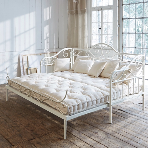 Canapé en métal blanc avec matelas crème et coussins dans une pièce lumineuse au sol en bois