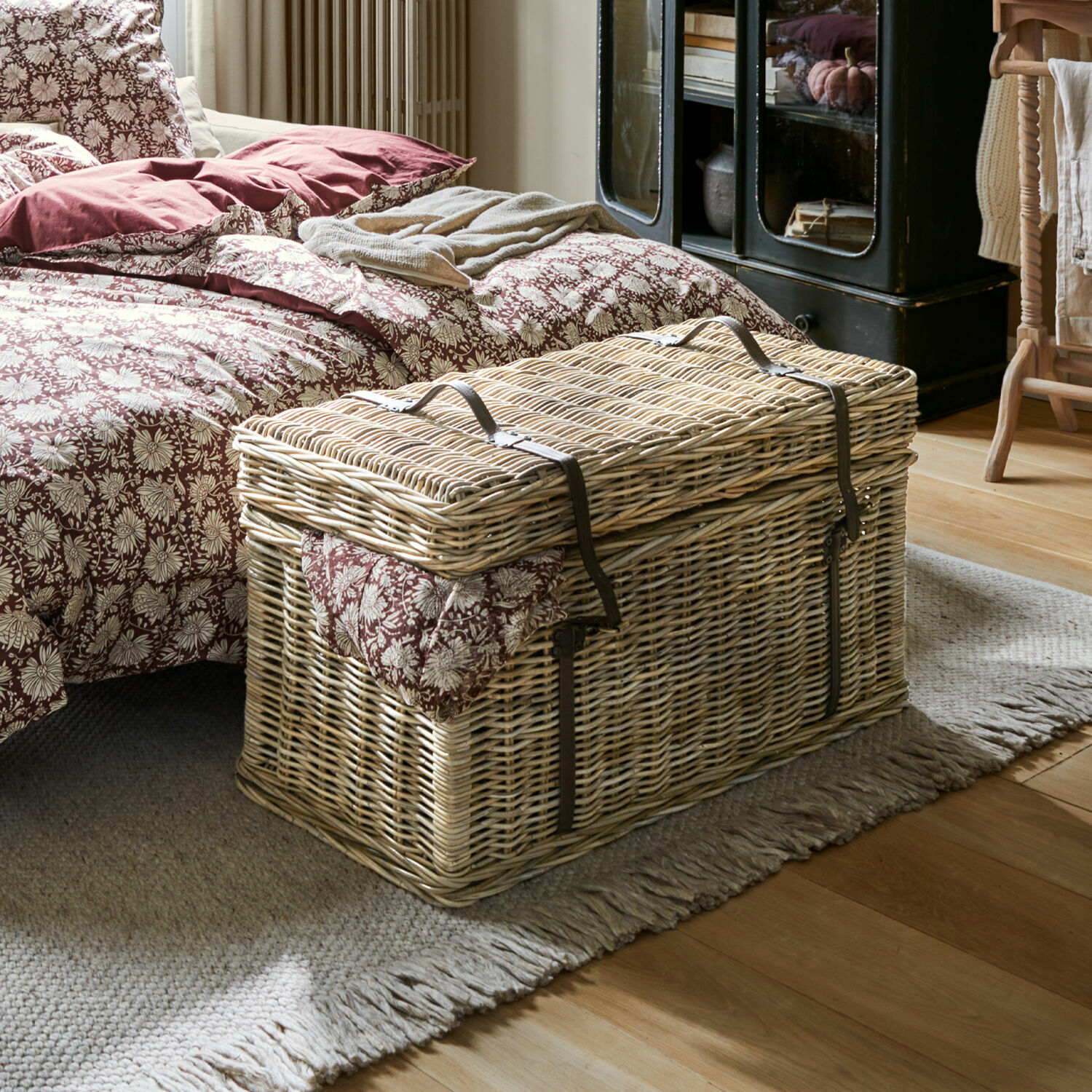 Malle Finette Grande malle en osier naturel avec sangles en cuir synthétique dans une chambre à coucher