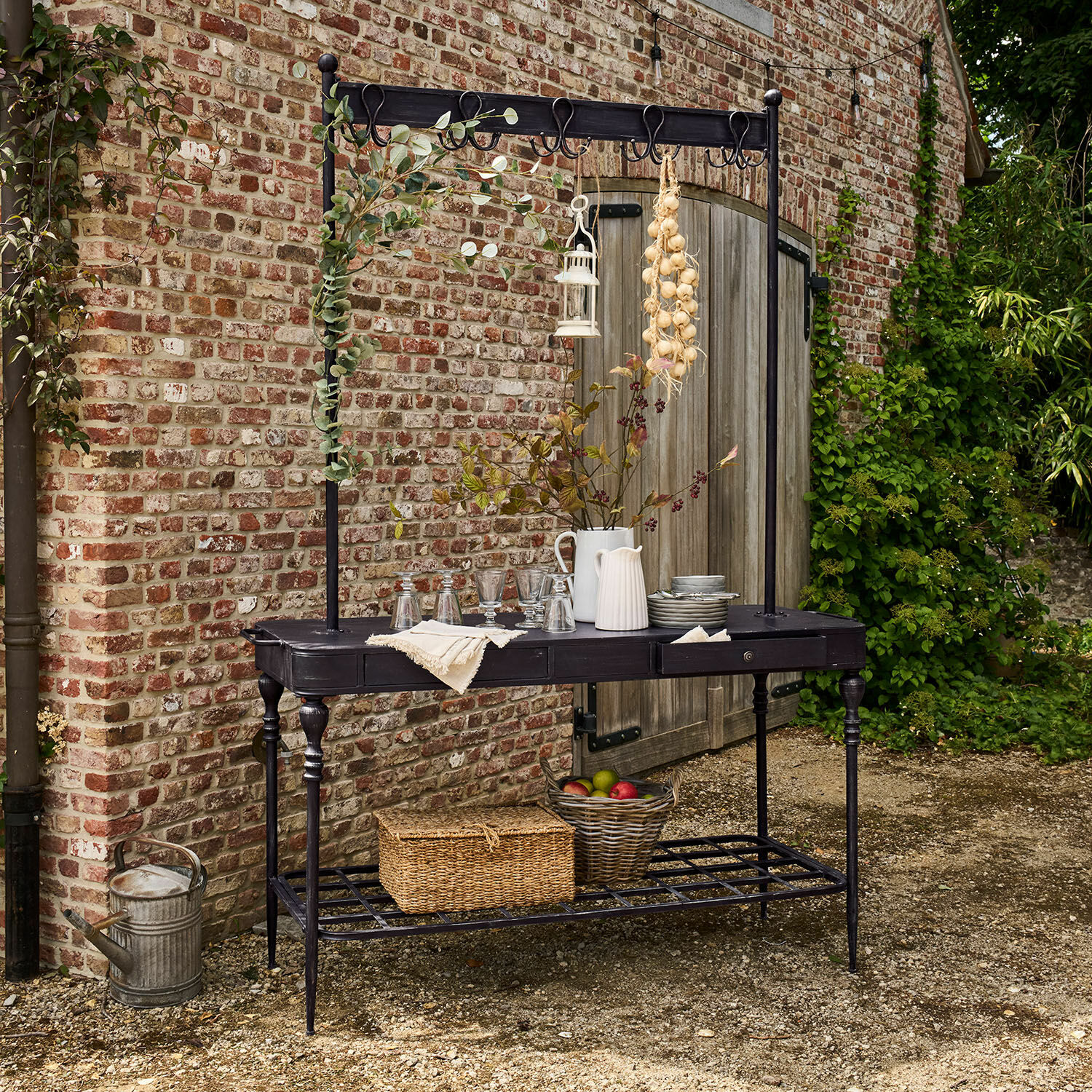 Console Langmore Table de jardin en métal noir avec crochets et étagère, décorée de pichets et panier de fruits