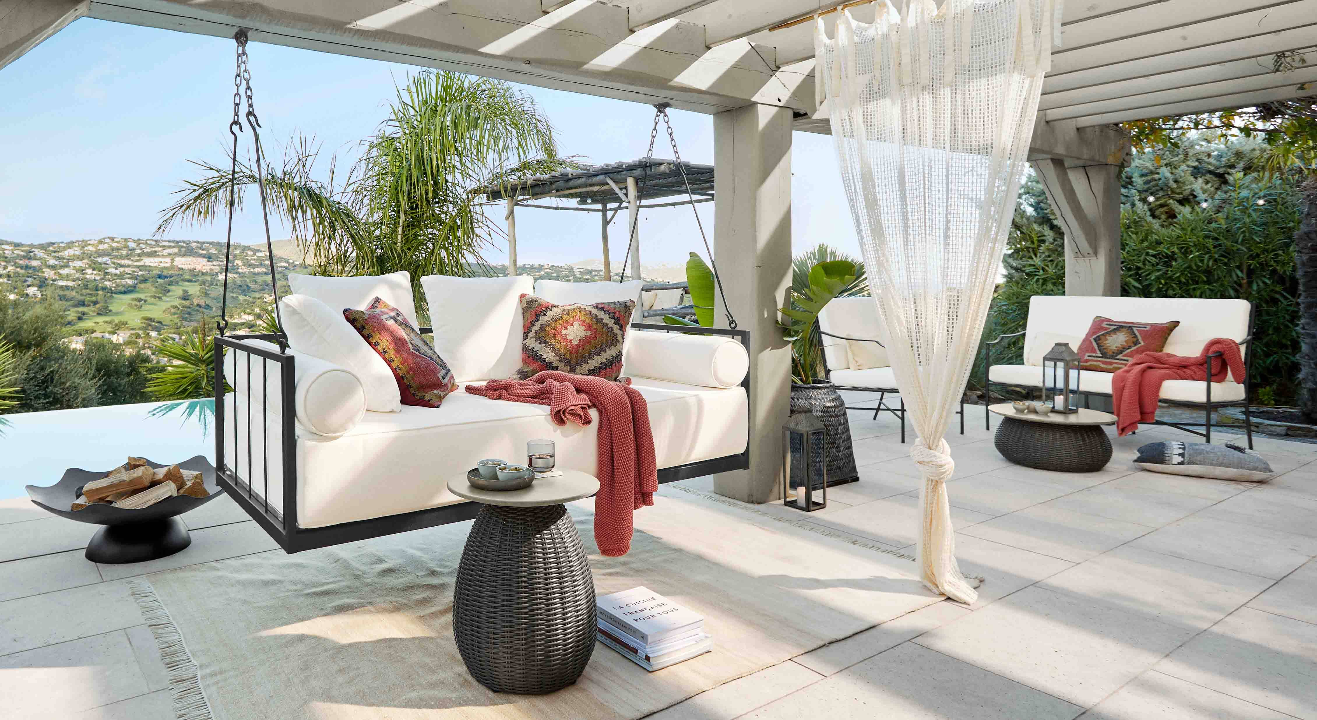 Canapé suspendu blanc avec cadre en métal et coussins colorés sur terrasse avec vue sur collines