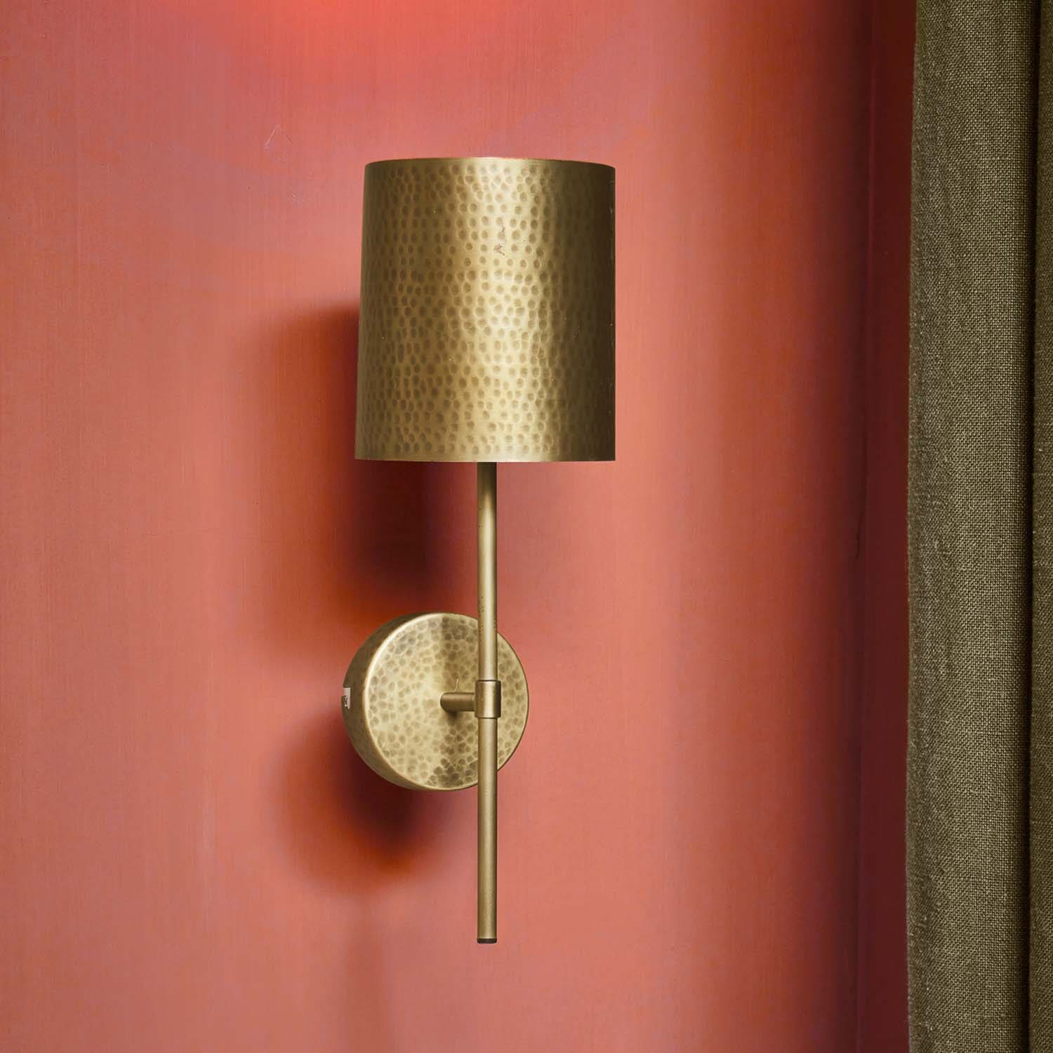 Applique murale en laiton martelé avec abat-jour cylindrique sur mur rouge, éclairage décoratif