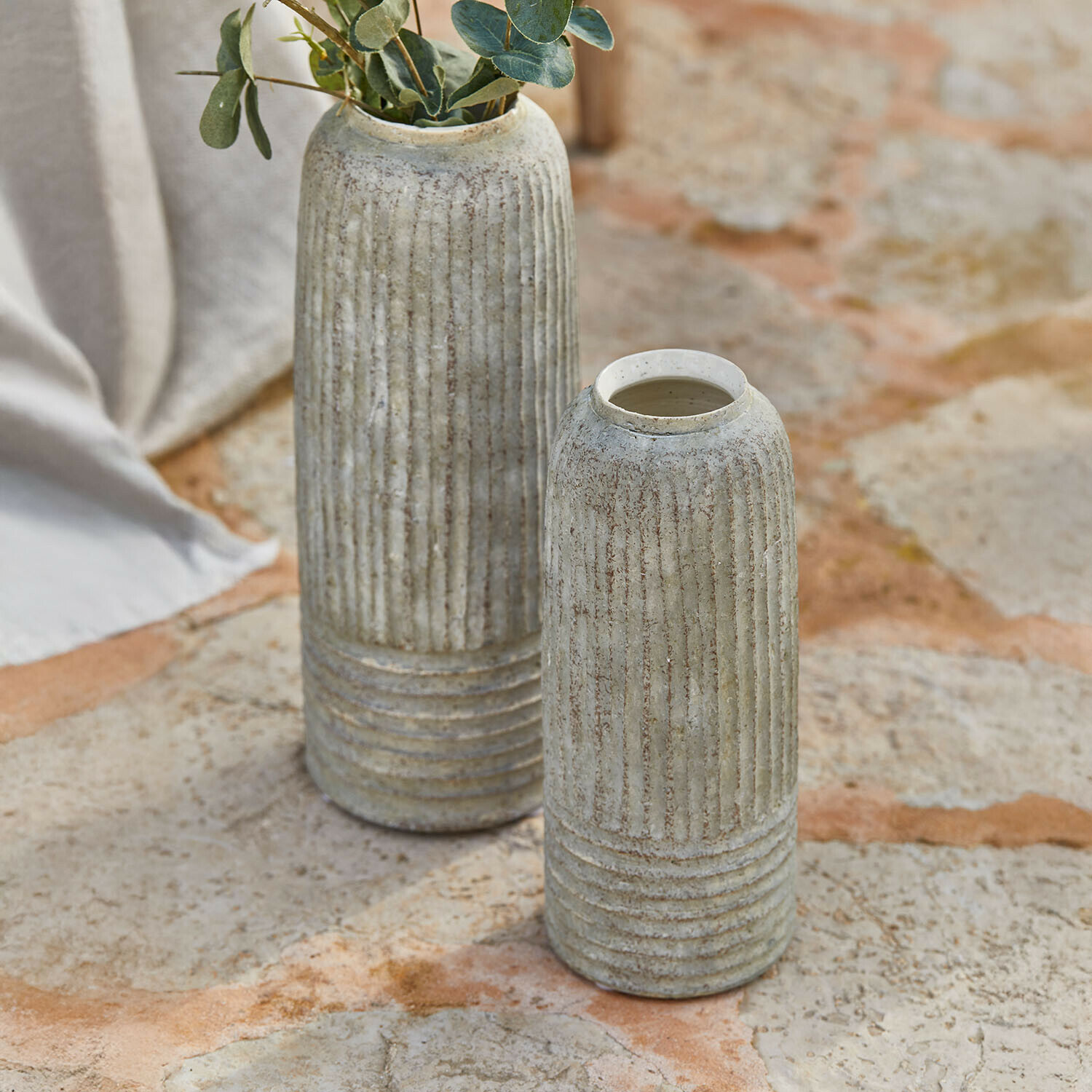 Deux vases en céramique grise avec rainures verticales posés sur un sol en pierre, décoration intérieure