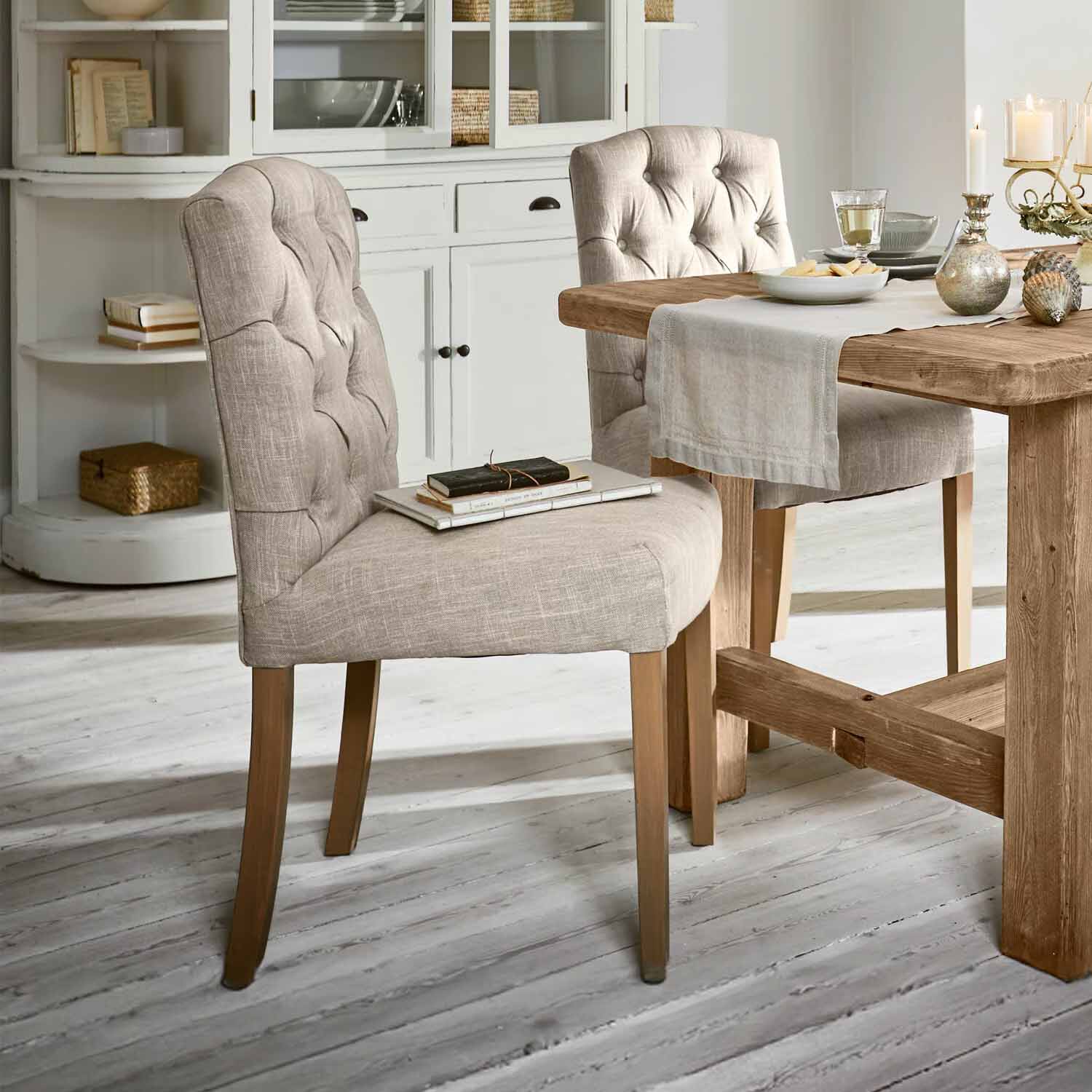 Chaise beige rembourrée avec pieds en bois près d'une table en bois dans une salle à manger lumineuse