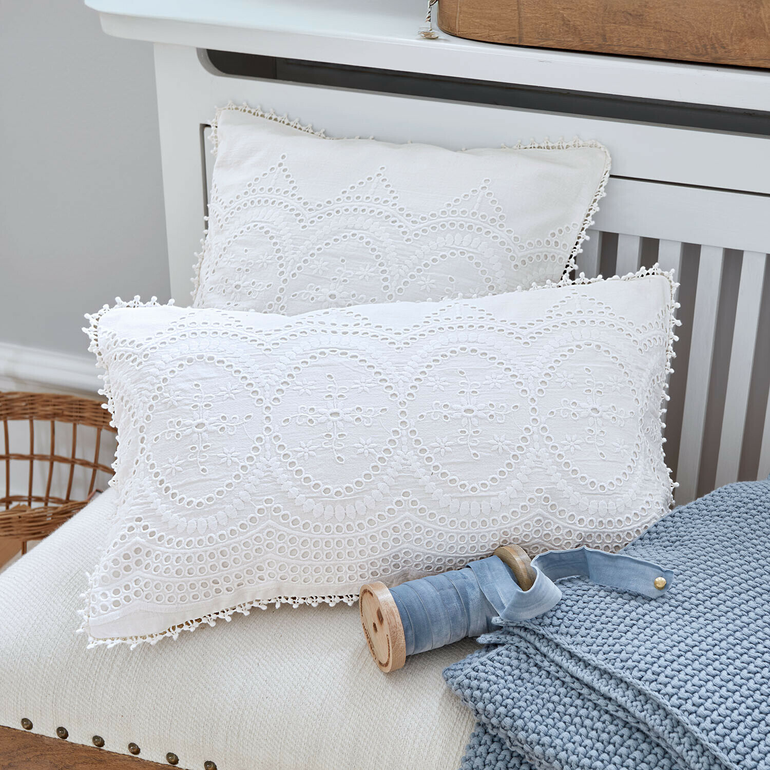 Lot de 2 housses de coussins Olyane Coussins blancs en coton avec broderie ajourée posés sur un canapé avec une couverture bleue