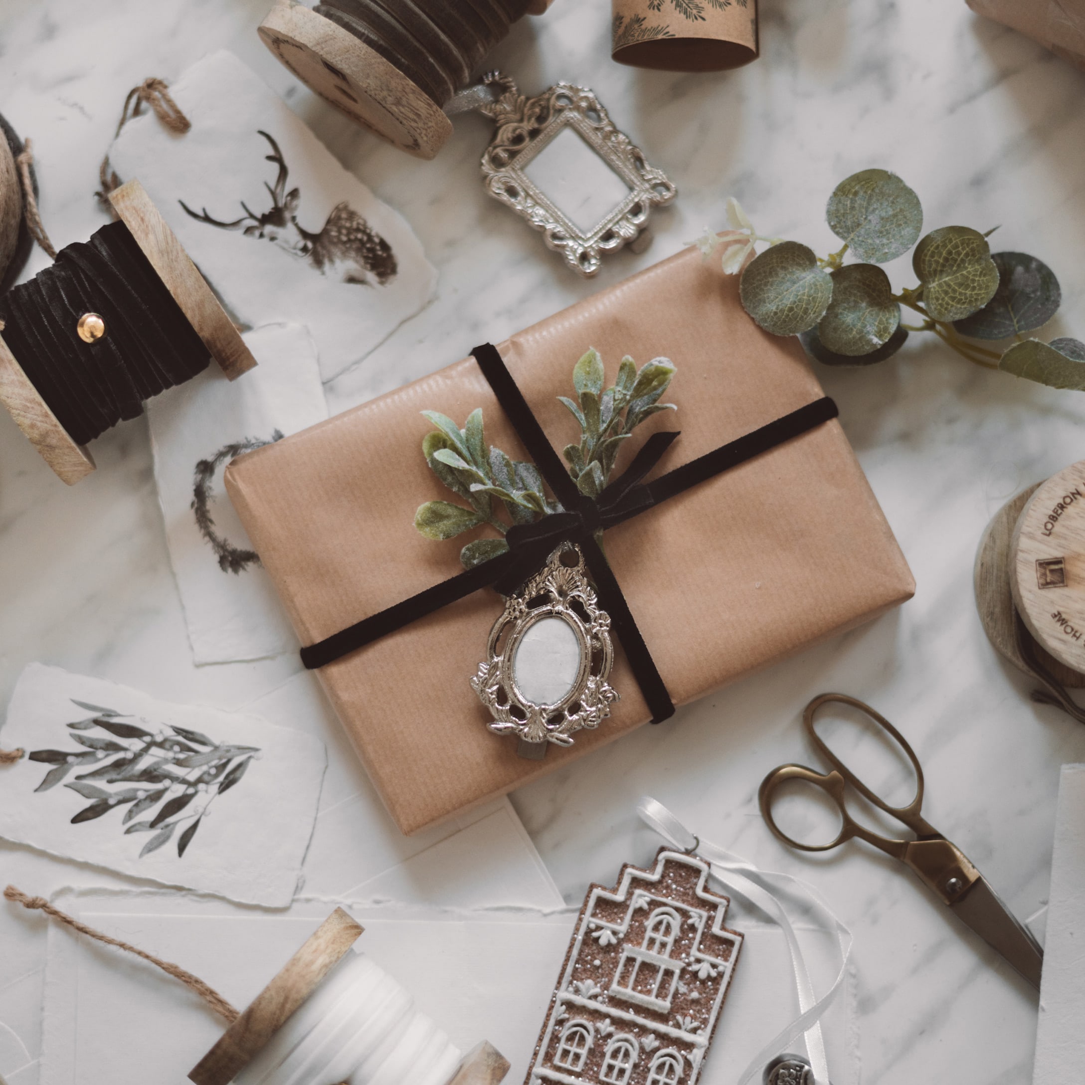Cadeau emballé dans du papier kraft marron avec ruban noir et feuillage vert sur fond en marbre avec décorations