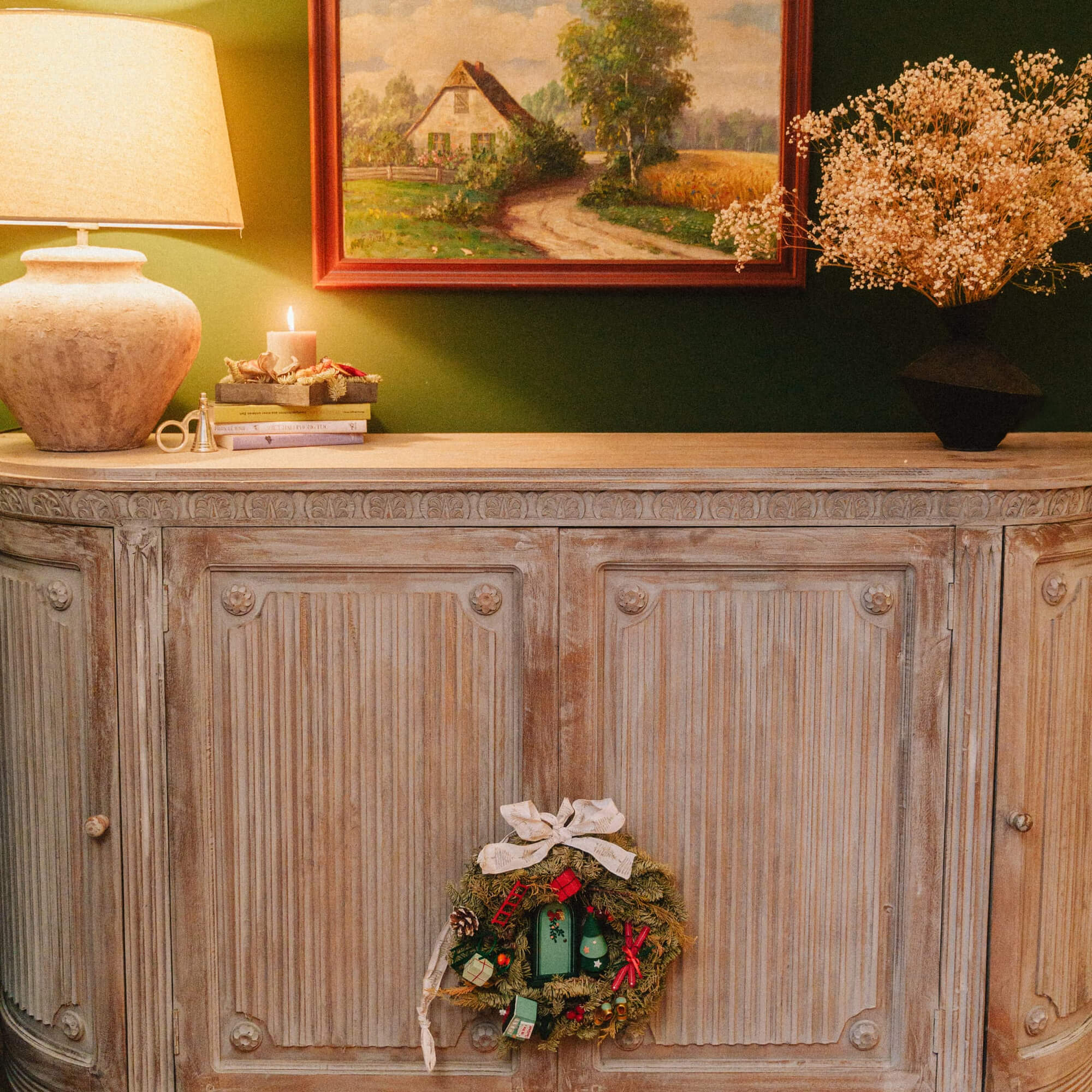 Buffet en bois vintage avec couronne de Noël verte et décorations sur le dessus dans une pièce chaleureuse