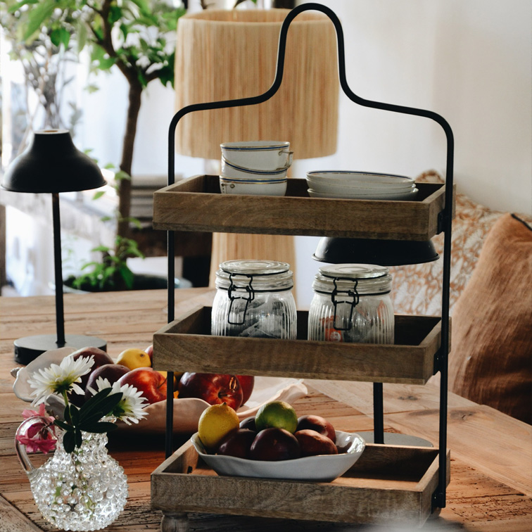Étagère à trois niveaux en bois et métal avec vaisselle et fruits sur une table rustique dans une salle à manger