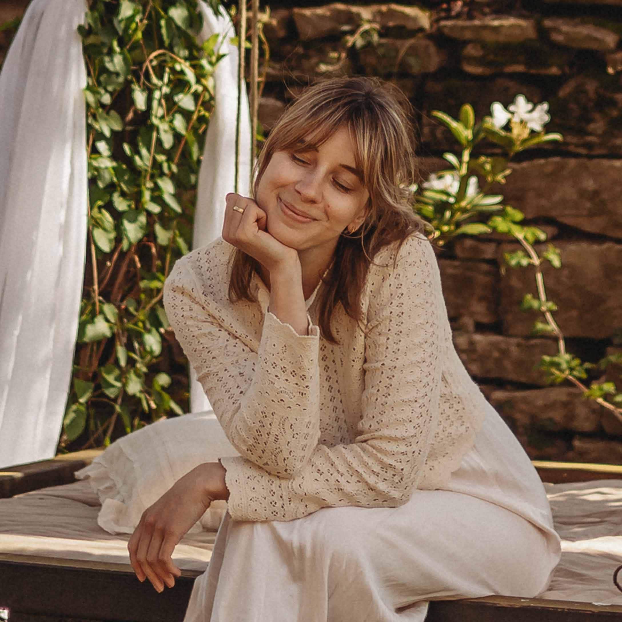 Femme en pull ajouré crème assise dehors sur un coussin dans un cadre naturel paisible