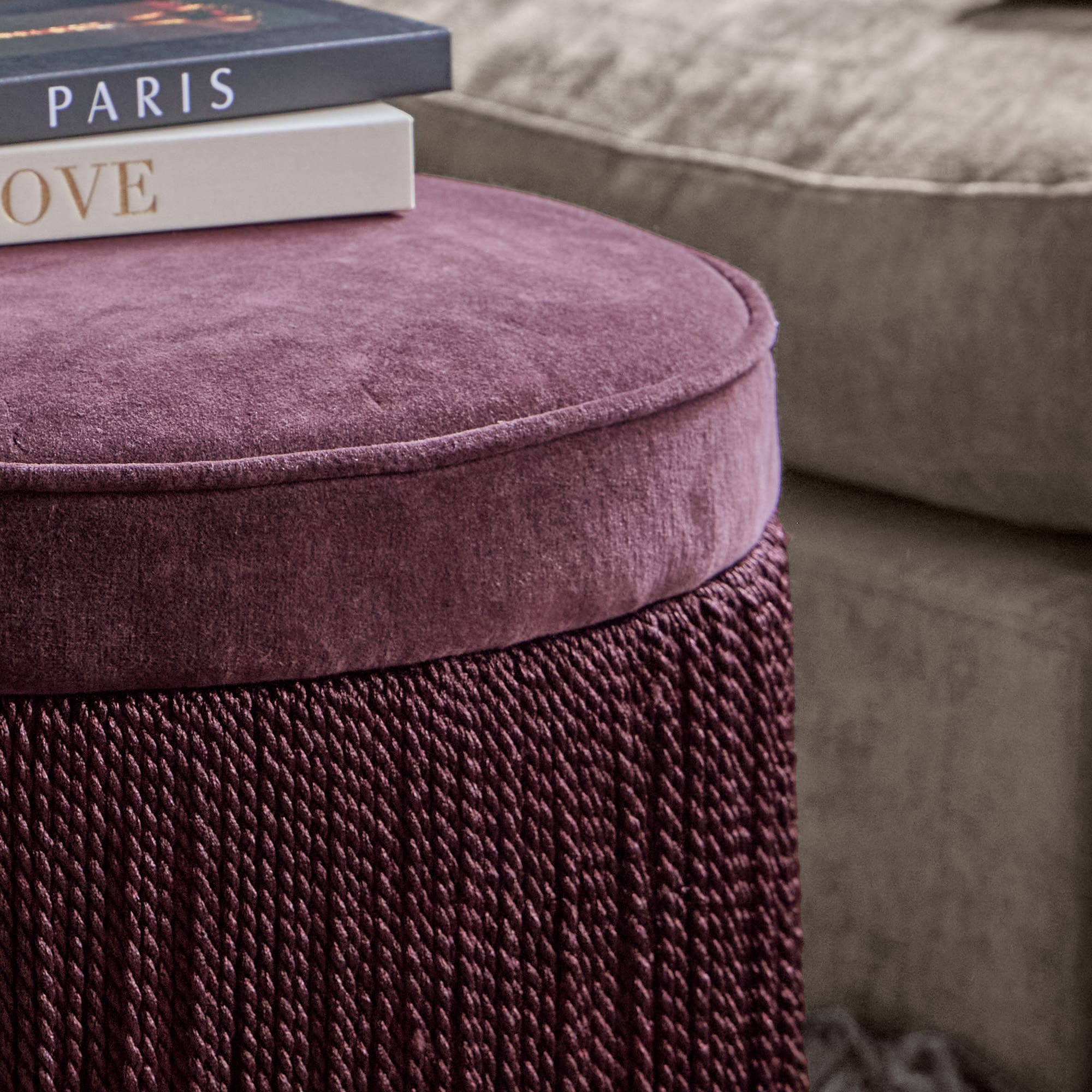Pouf violet en velours doux et tissu tressé avec canapé gris et livres en arrière-plan