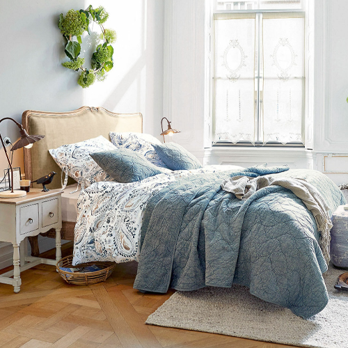 Chambre confortable avec couette matelassée bleue et linge de lit à motifs sur lit à tête de lit beige