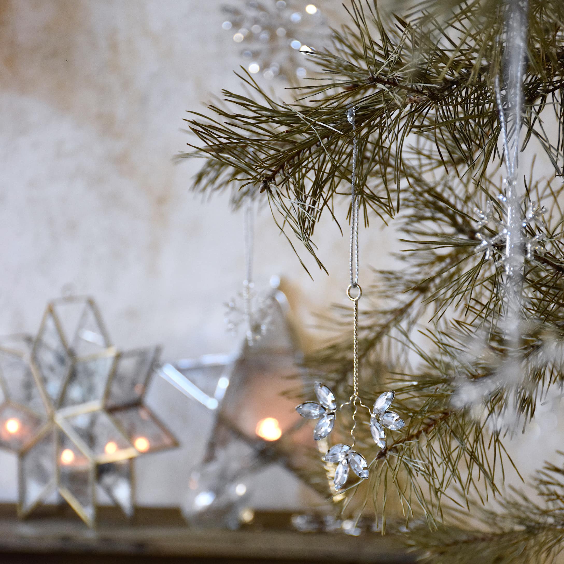Décoration de Noël en cristaux transparents suspendue à une branche de sapin avec lanternes en arrière-plan