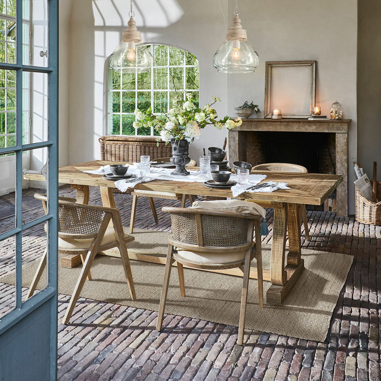 Table Campbelltown Salle à manger avec table en bois et chaises en osier sur sol en briques avec décoration florale