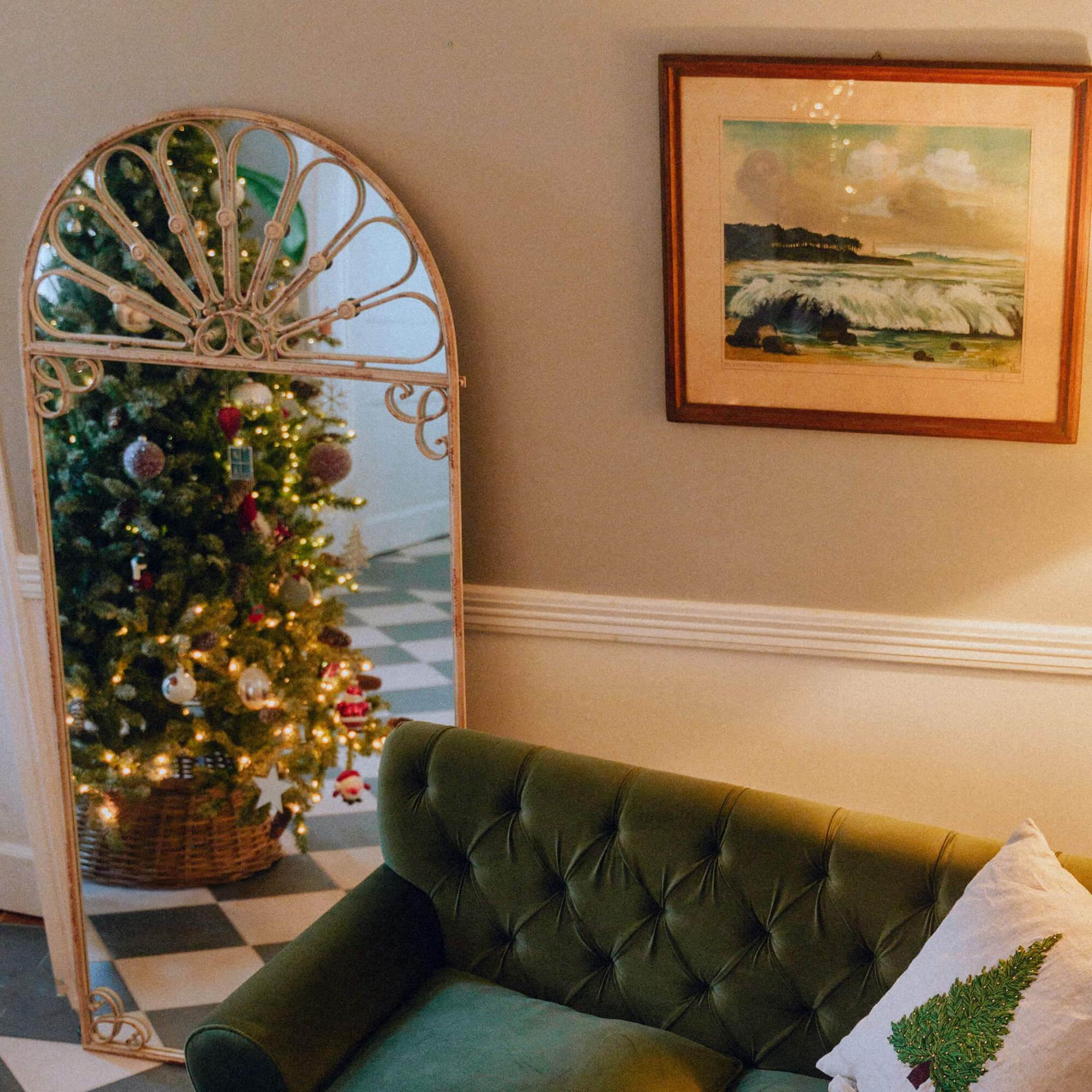 Miroir vintage en métal reflétant un sapin de Noël décoré et un canapé vert avec coussin décoratif