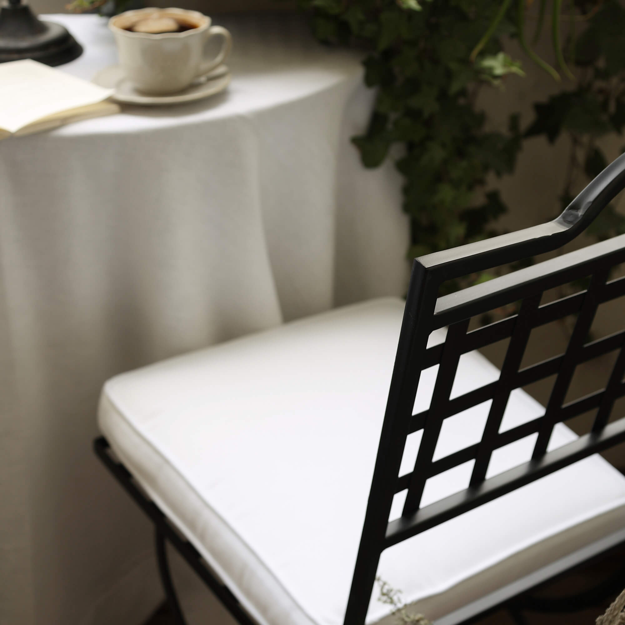 Chaise en métal noir avec coussin blanc près d'une table avec tasse de café et plantes vertes sur balcon